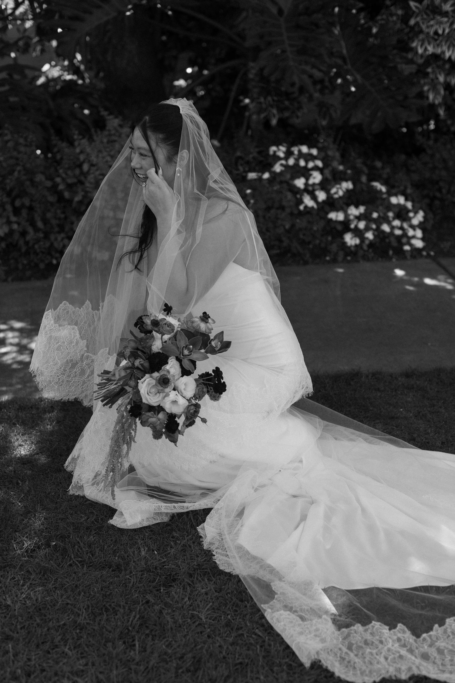 Black and white photo of a bride's dress and veil spread elegantly on grass with flowers.