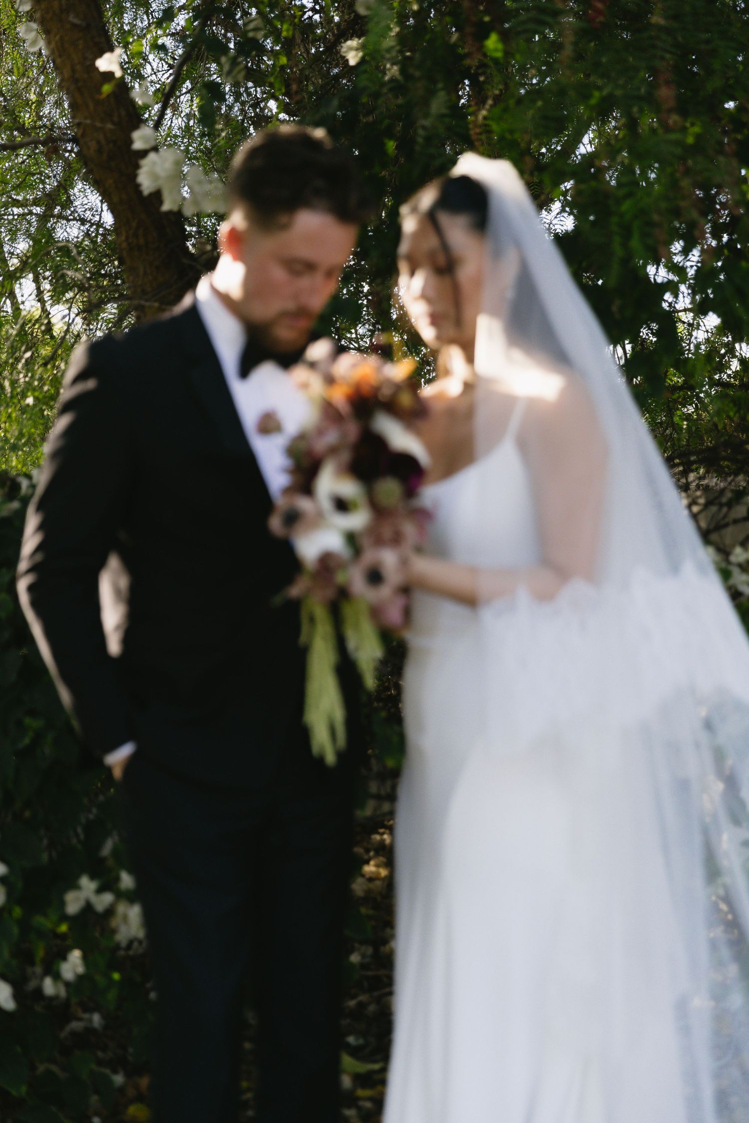 Wedding couple sharing intimate moments under trees during outdoor photo session.