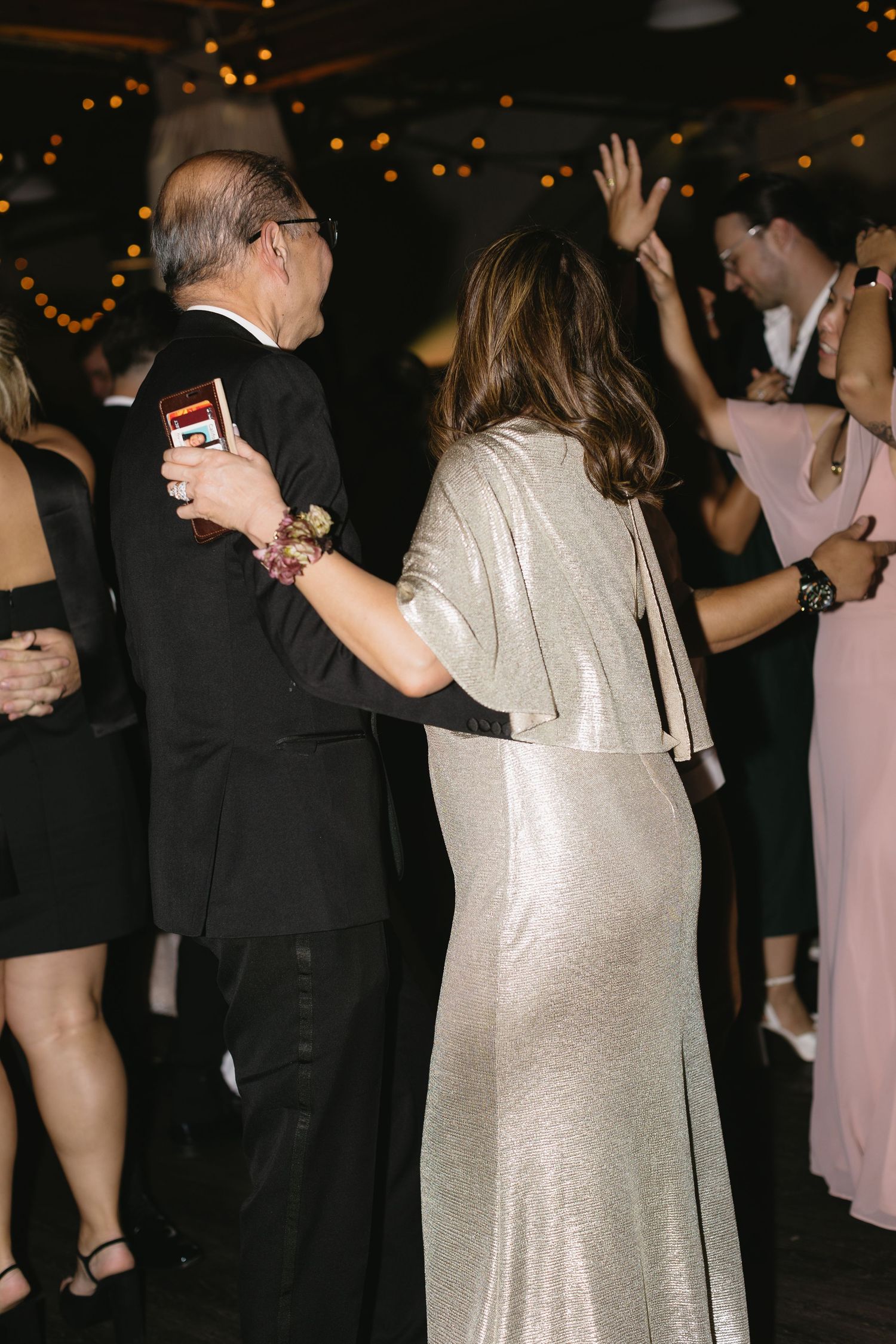 Wedding guests dancing and celebrating at dimly lit reception venue.
