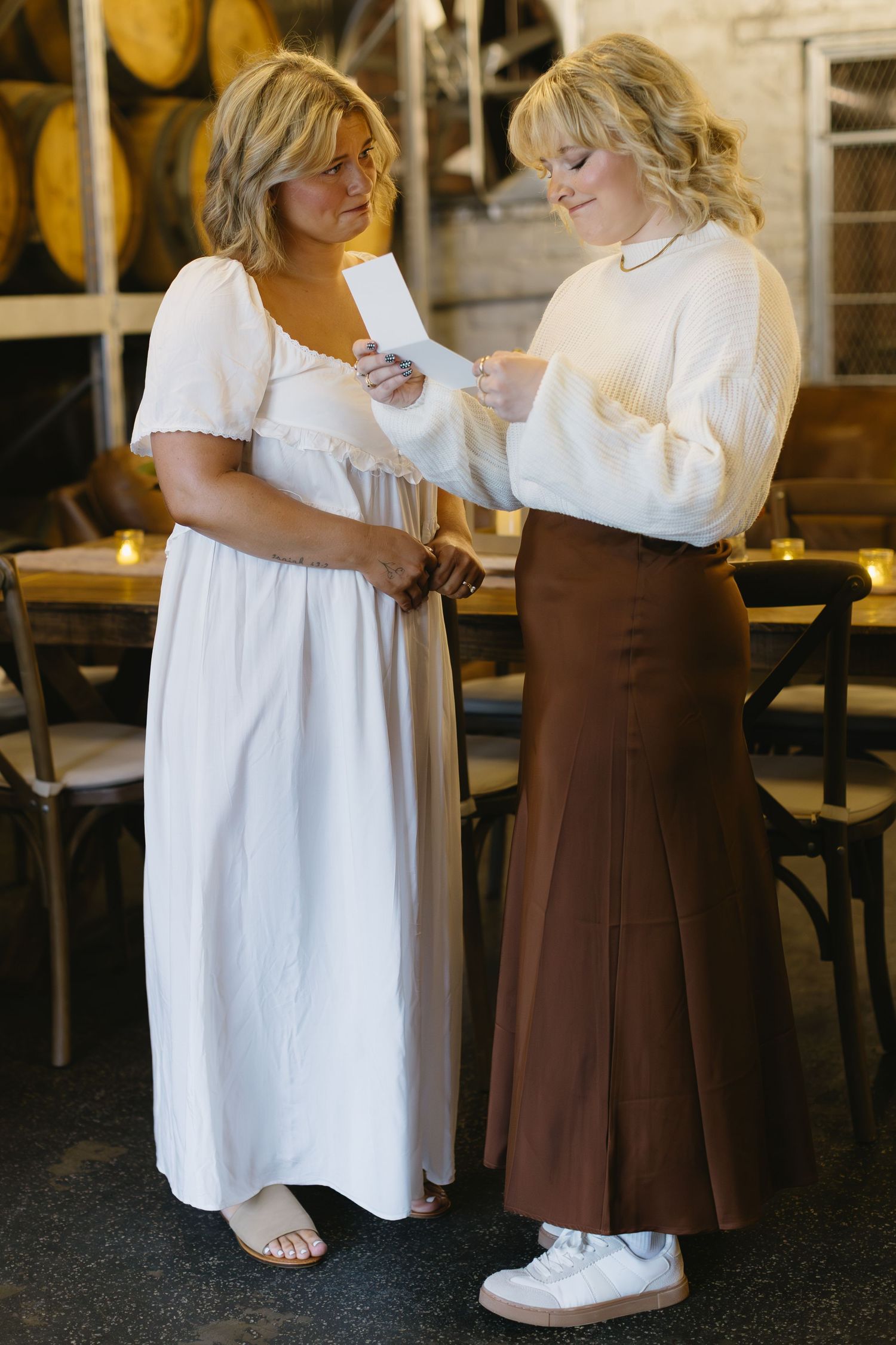 Two people in white and brown outfits sharing a playful moment on a dark floor.