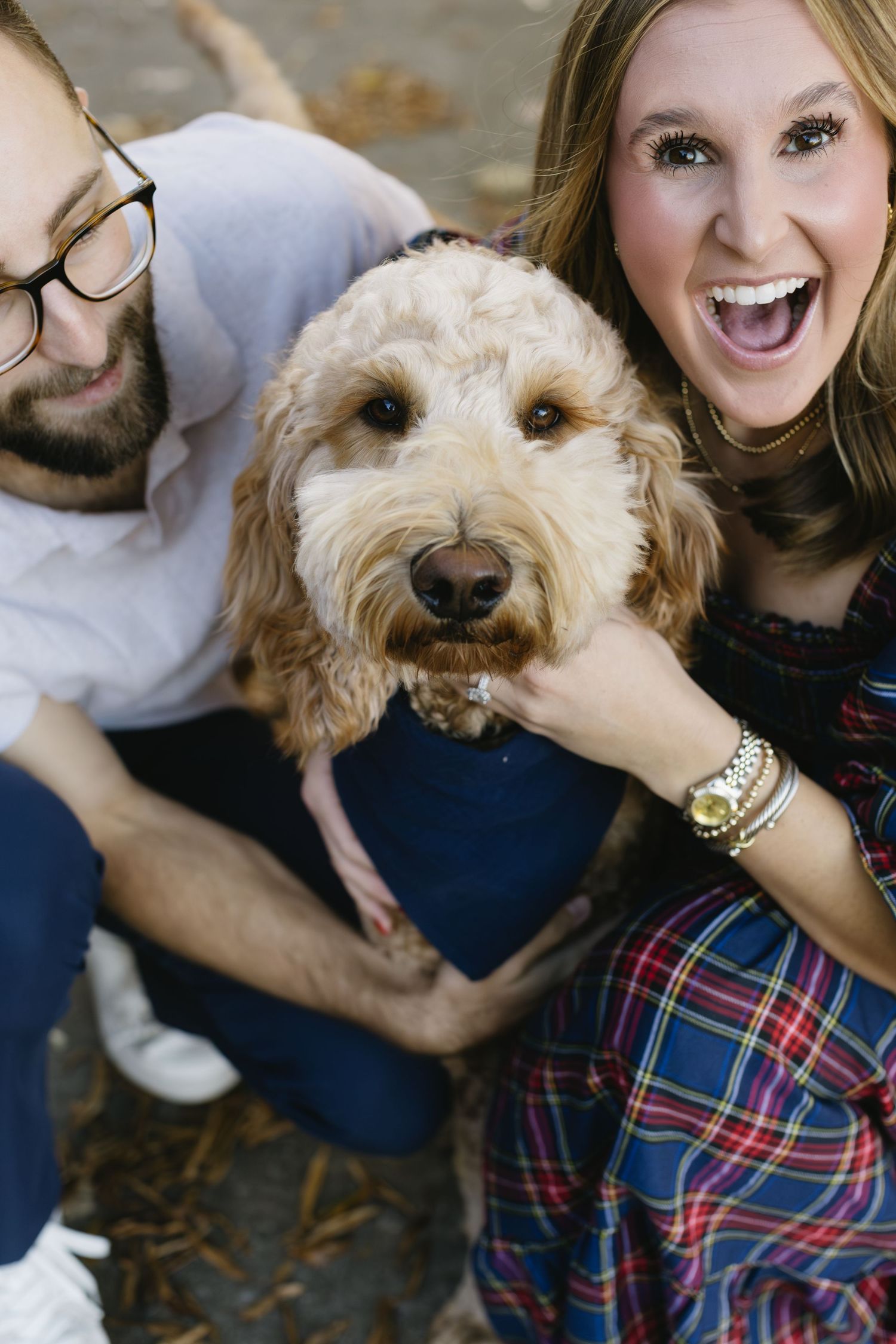 A goldendoodle dog poses playfully with its owners during an outdoor autumn photoshoot.