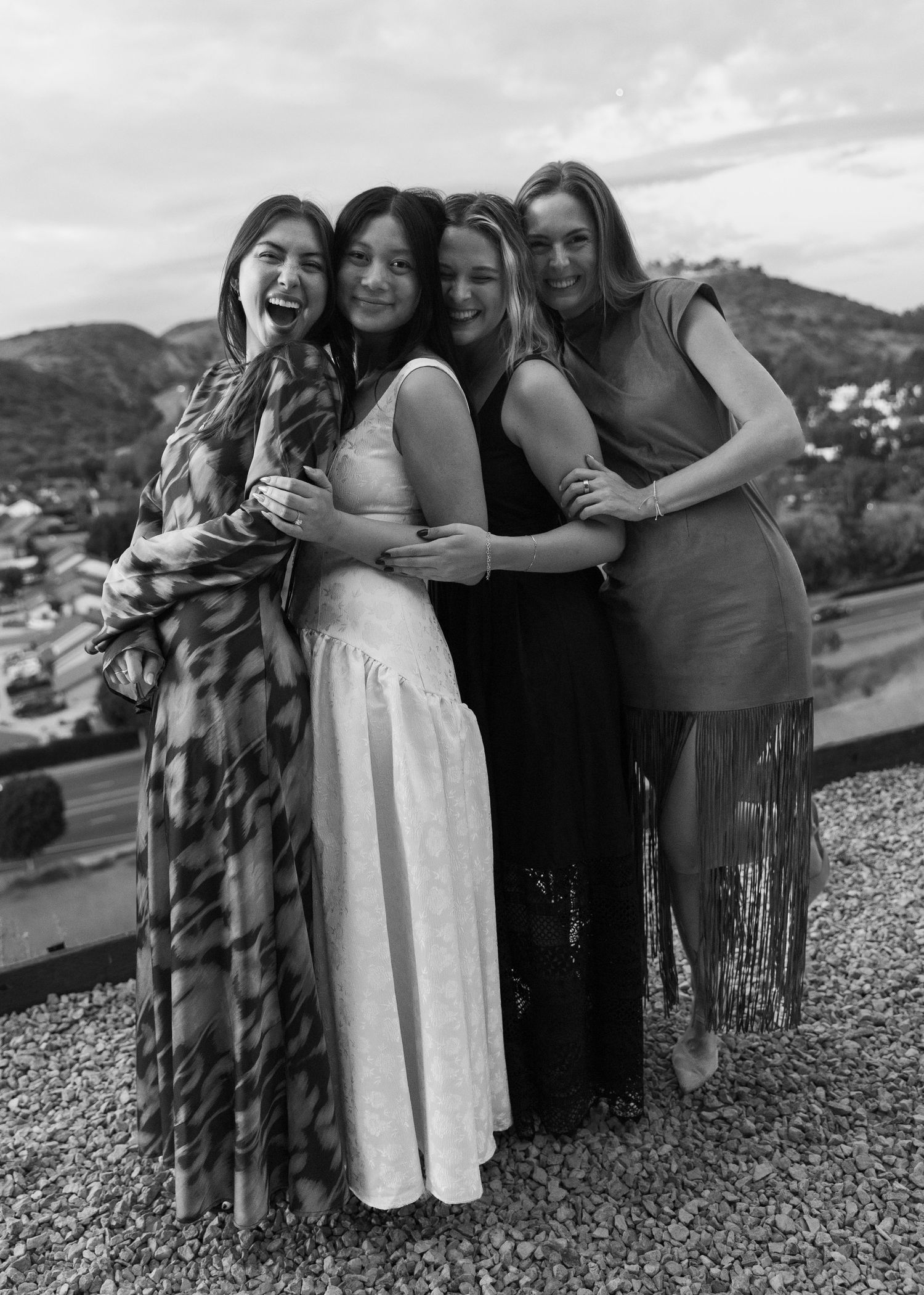 A group of friends embrace and laugh together on a hilltop overlook during a black and white photoshoot.