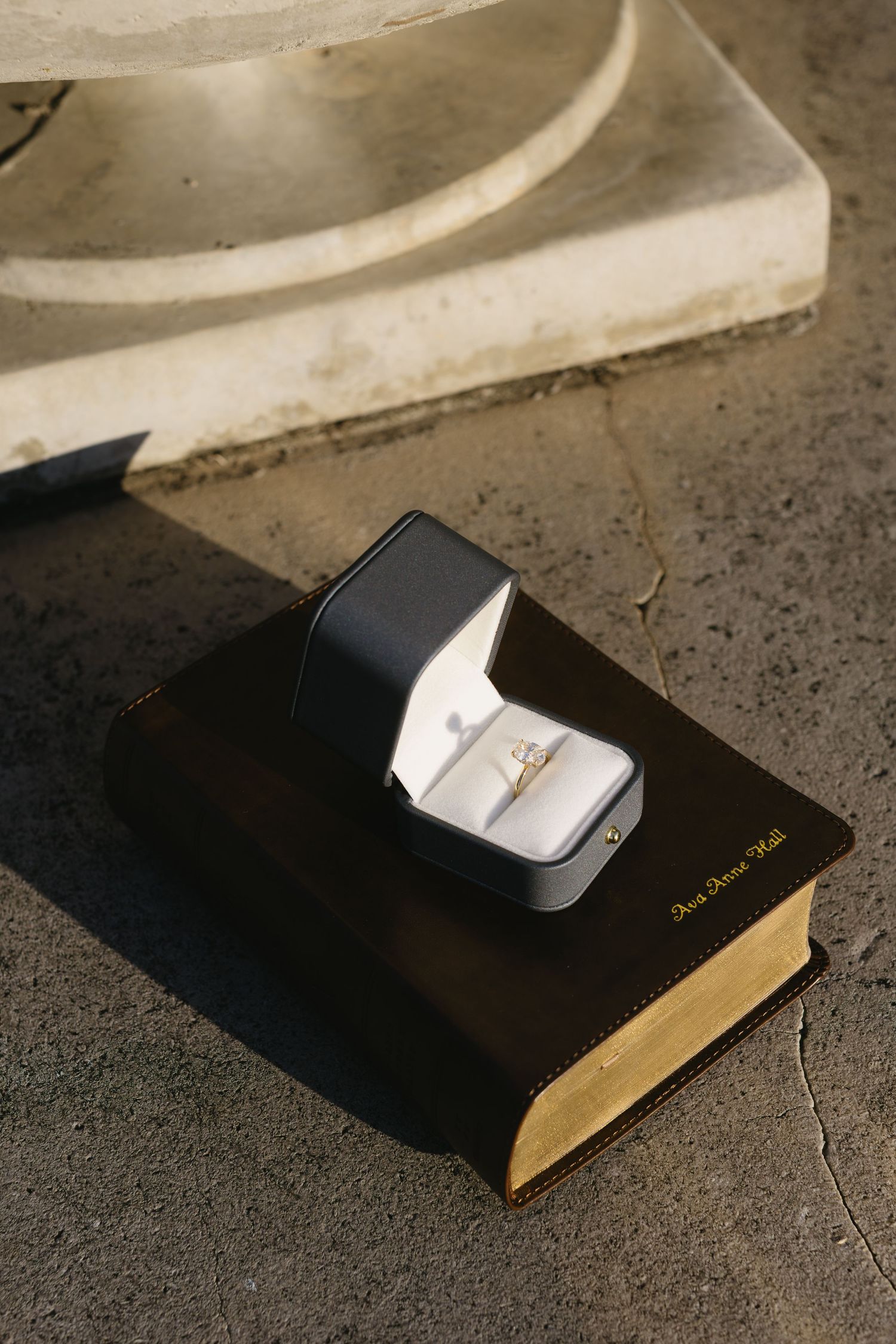 A black book with a white ring box placed on top photographed in dramatic lighting.