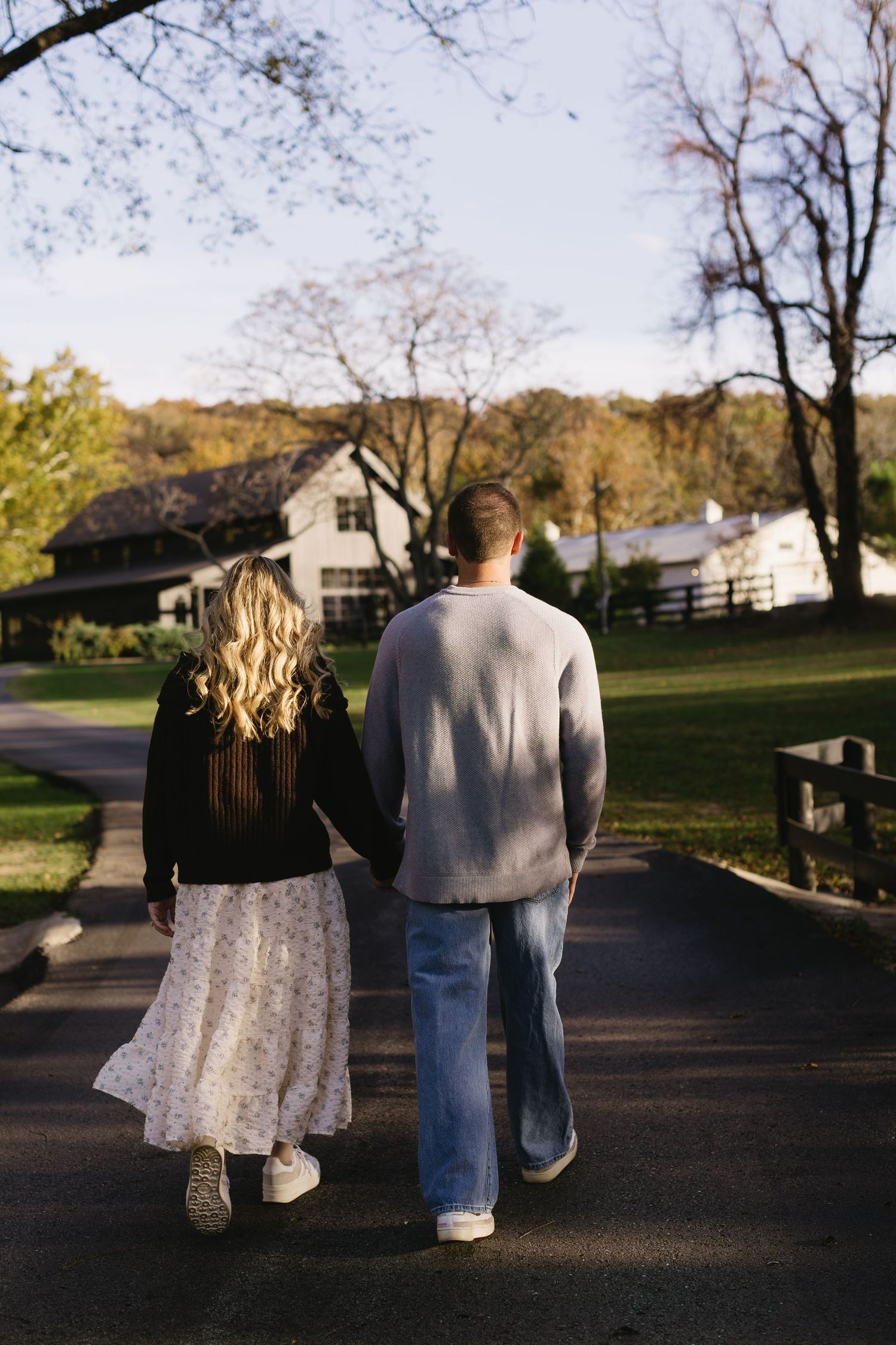 Couple walking together on a path at sunset with houses in background.