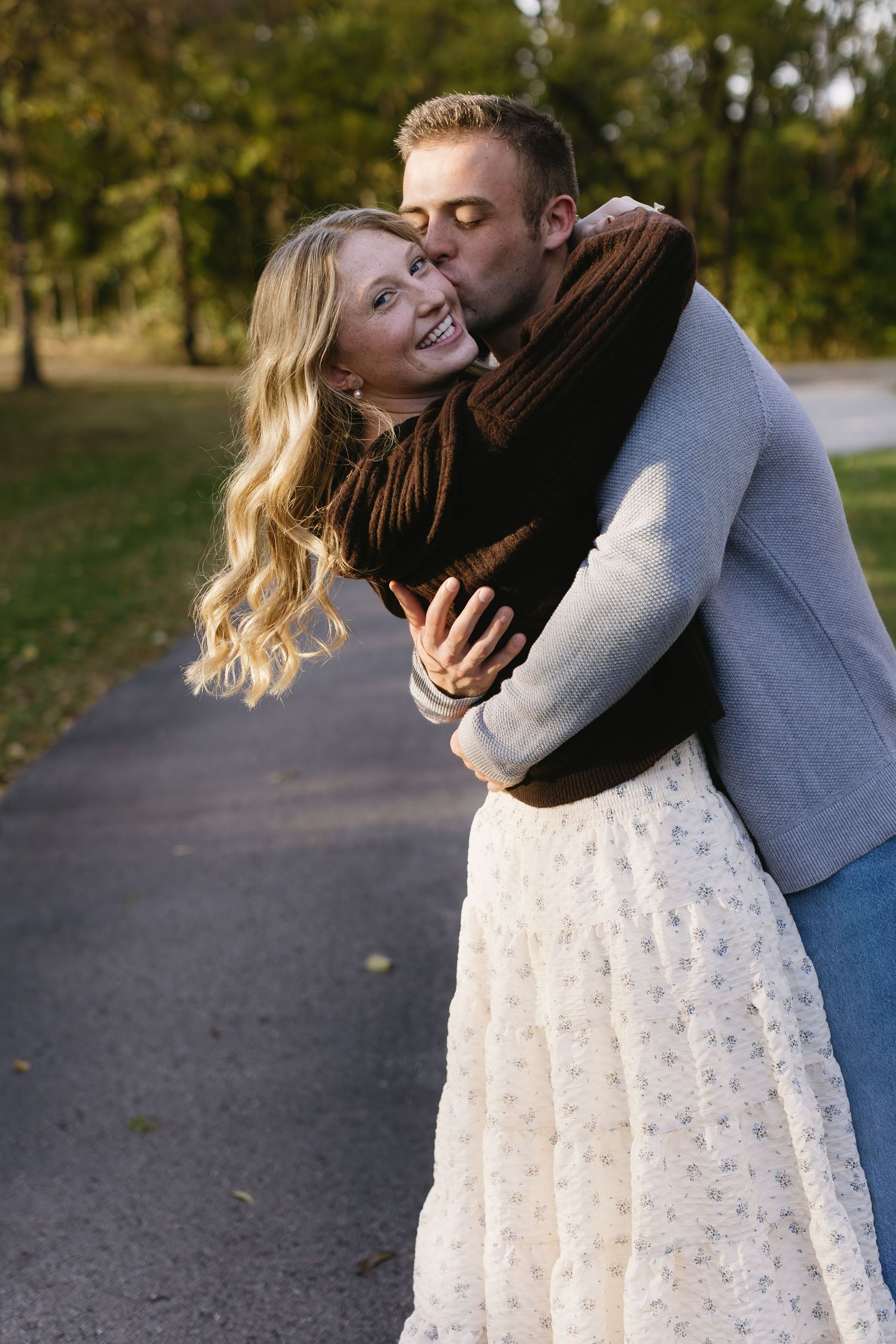 A romantic autumn photoshoot showing intimate moments between a couple on a park path.