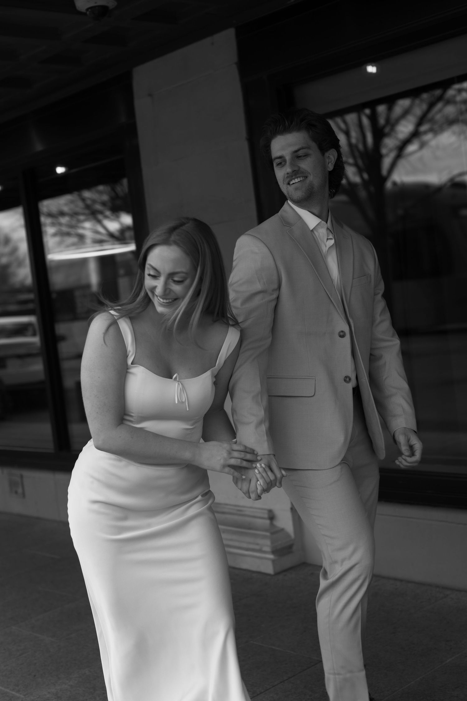 A couple in white dress and beige suit share candid moments in black and white photography.