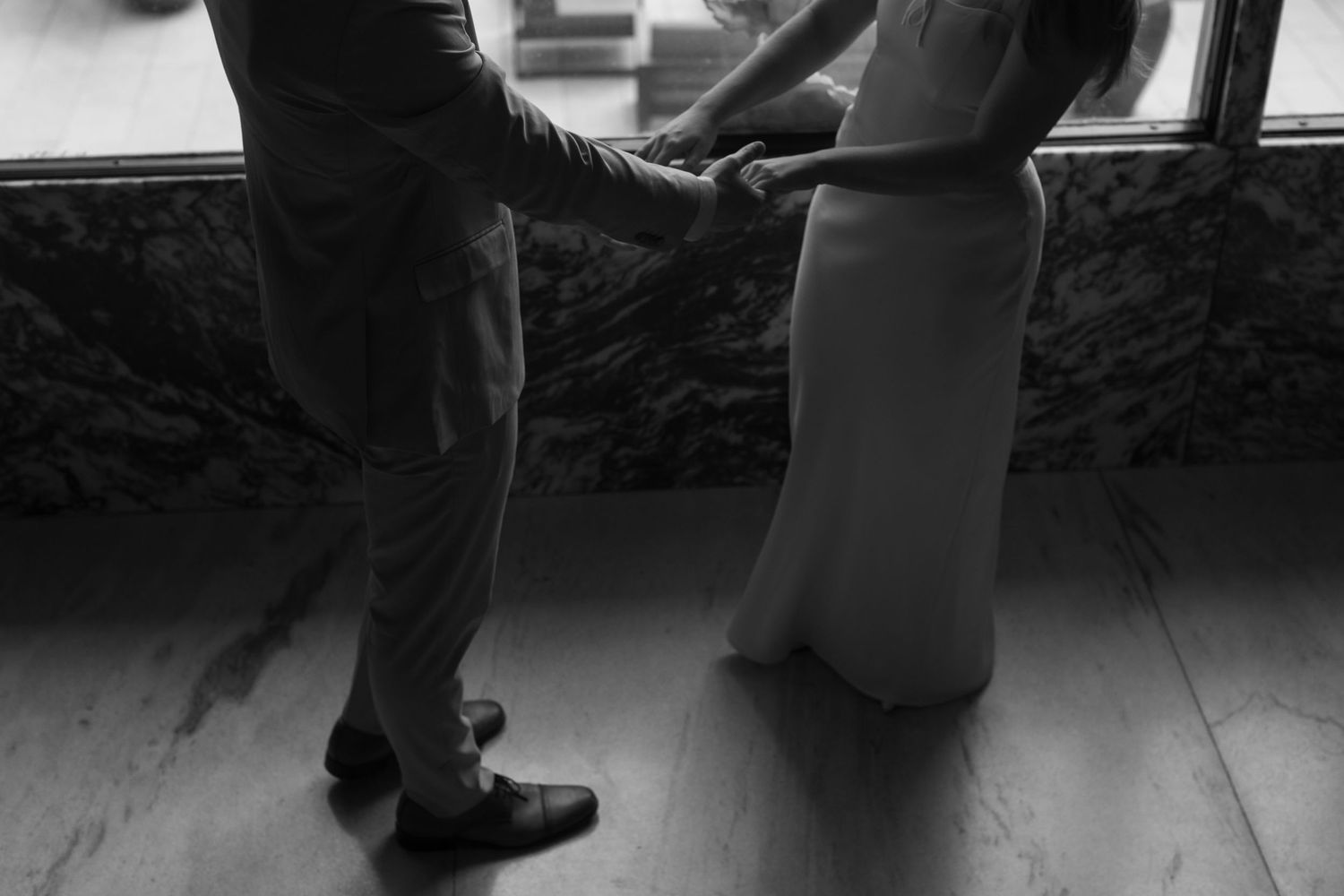 Black and white detail shot of formal shoes and dress hem on a dark floor.