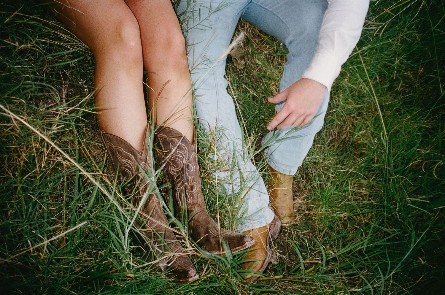 A repeating pattern shows leather cowboy boots and blue jeans walking through tall grass in a field.