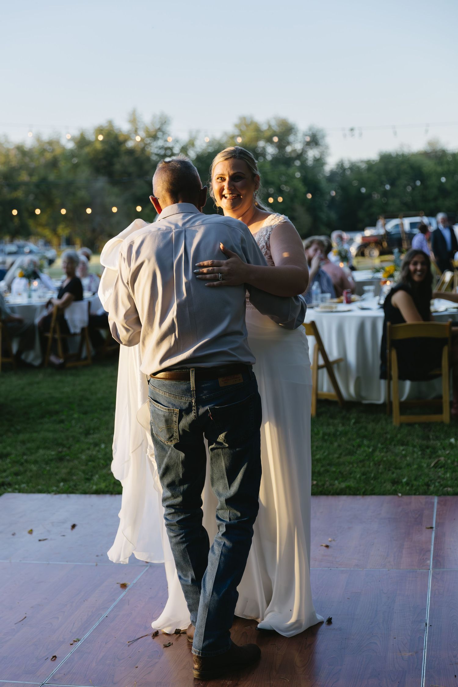 A couple shares their first dance on a wooden dance floor at an outdoor reception.