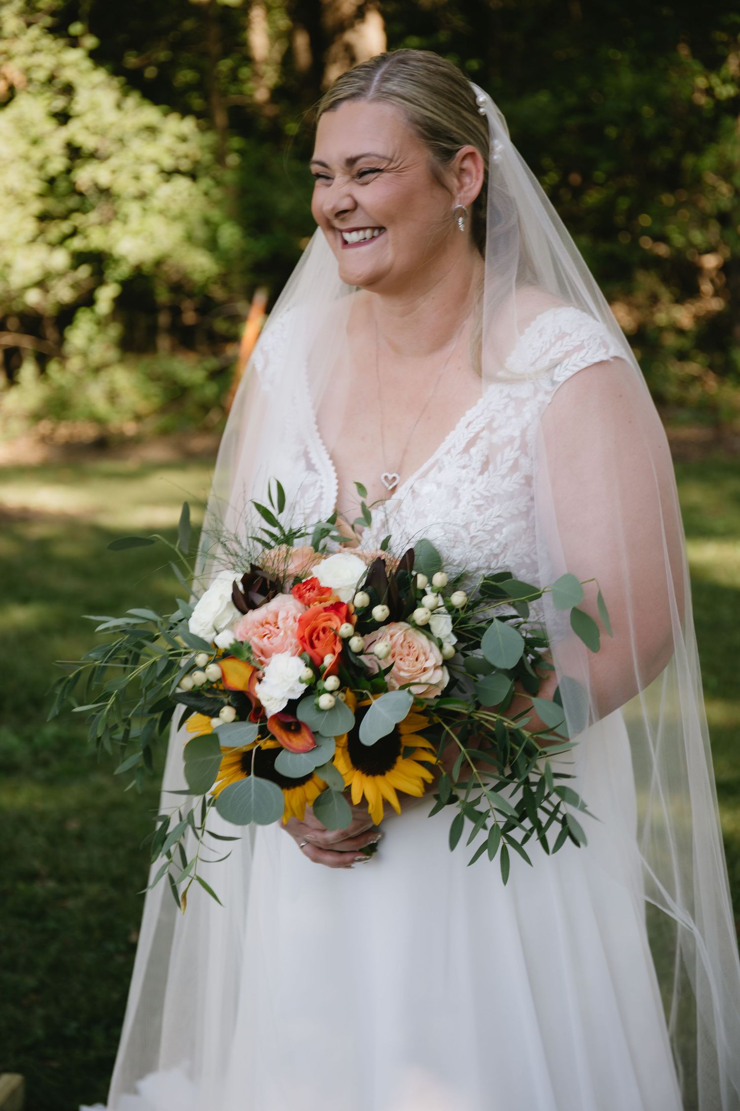 Bride in white dress holding vibrant sunflower and eucalyptus bouquet in outdoor garden setting.