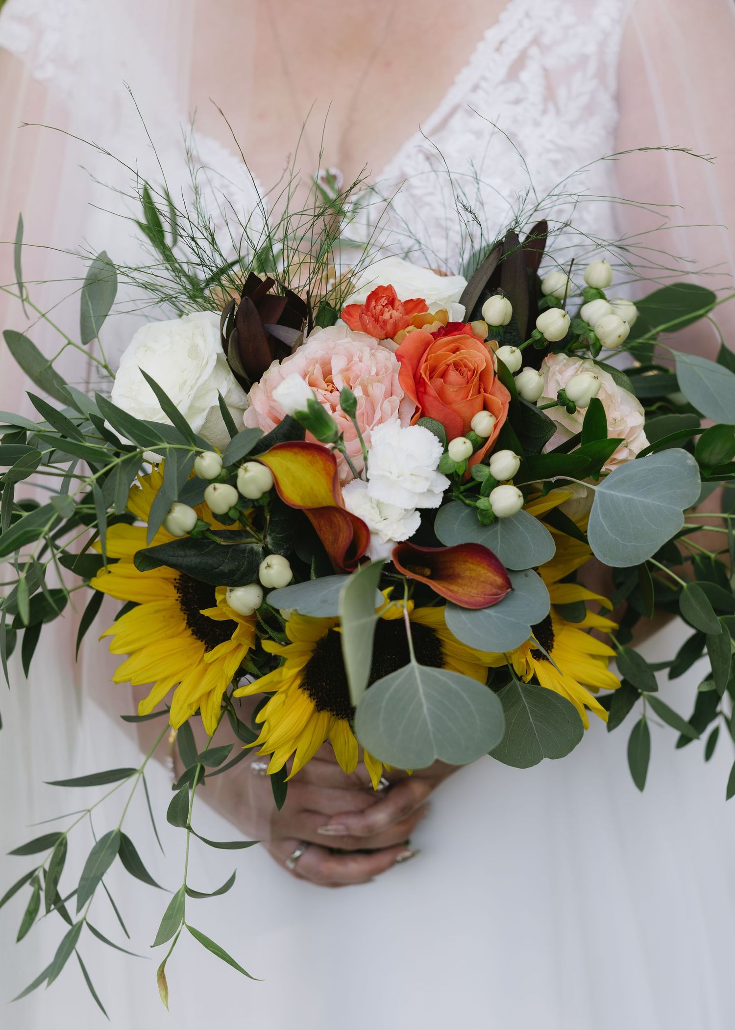 Vibrant bridal bouquet featuring sunflowers, coral roses, and eucalyptus leaves with white accents.
