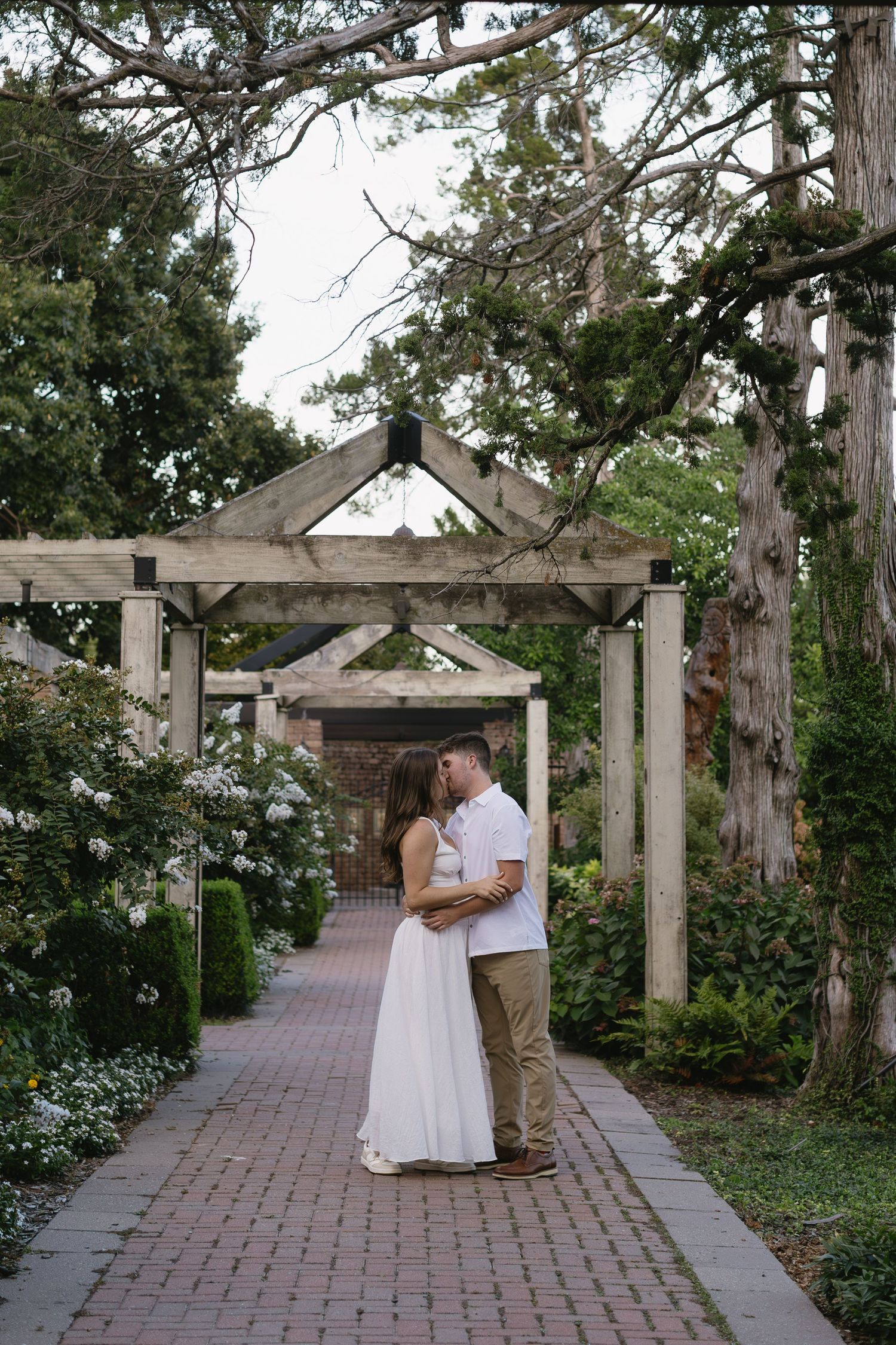 A couple shares intimate moments under a wooden garden pergola during their engagement shoot.