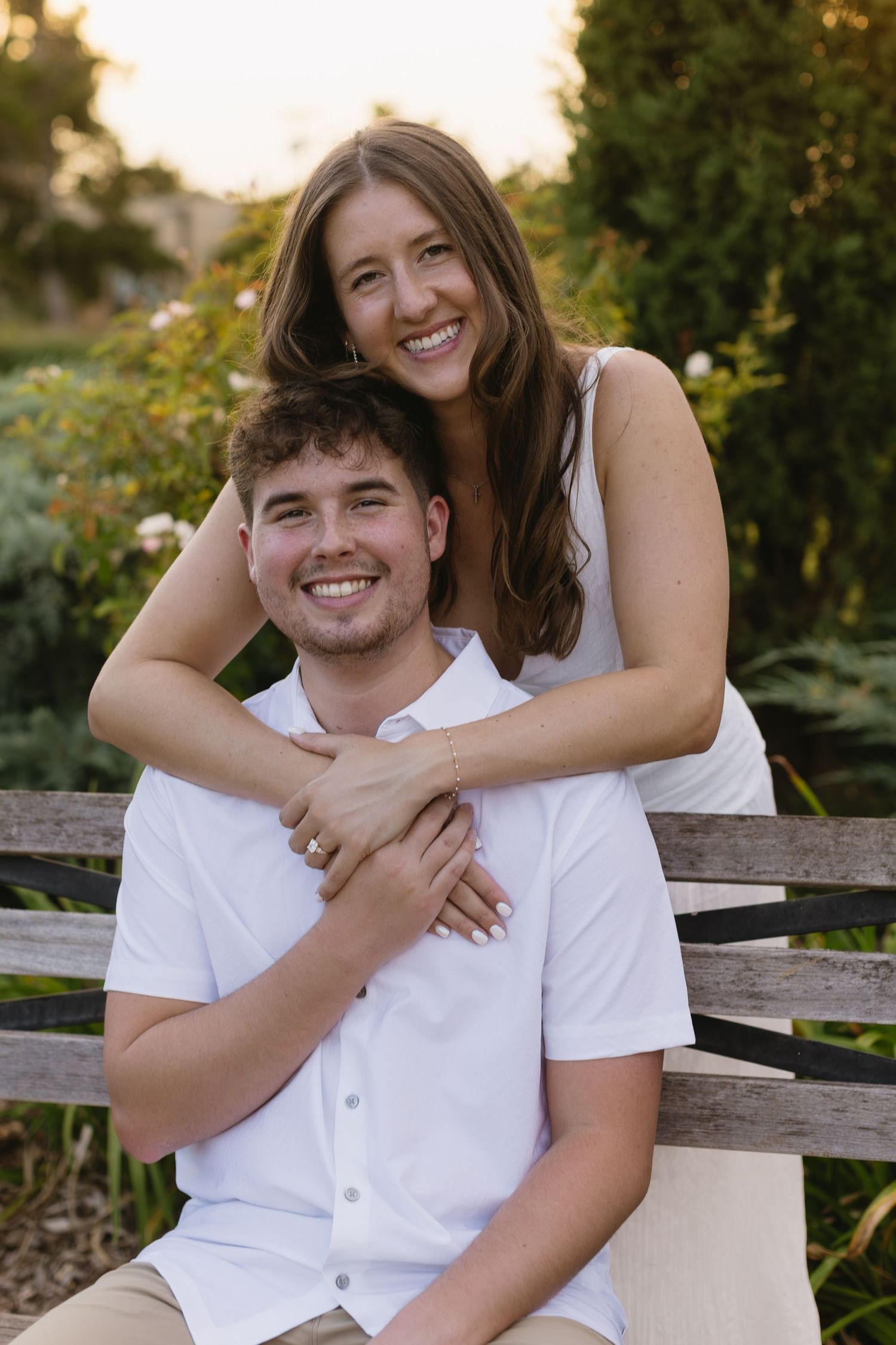 A couple enjoys candid moments together on a wooden bench in a garden setting.