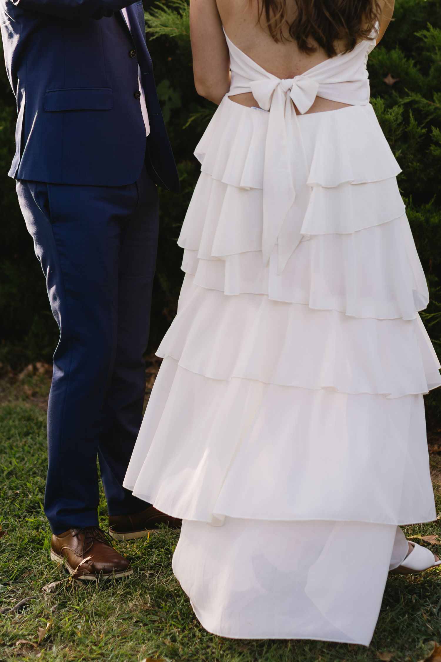 Close-up details of a layered white wedding dress with ruffles shown alongside sections of a navy blue suit and brown shoes.