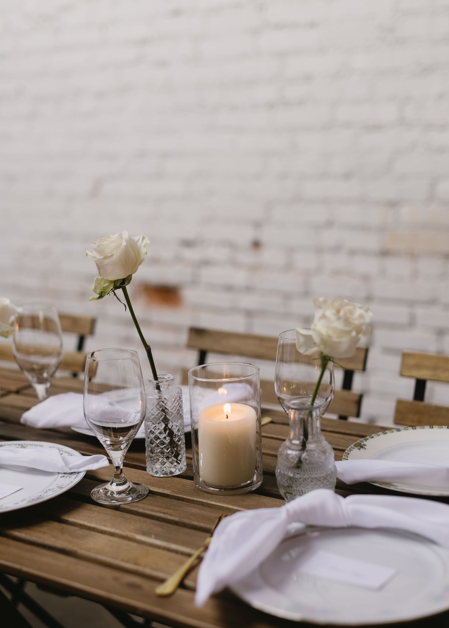 Elegant table setting with white candles, flowers and place settings on a rustic wooden table.