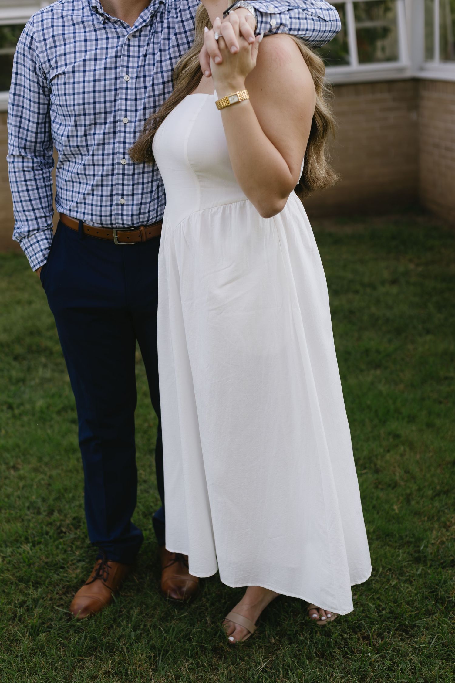 A couple in blue plaid and white dress poses together on a grassy lawn.