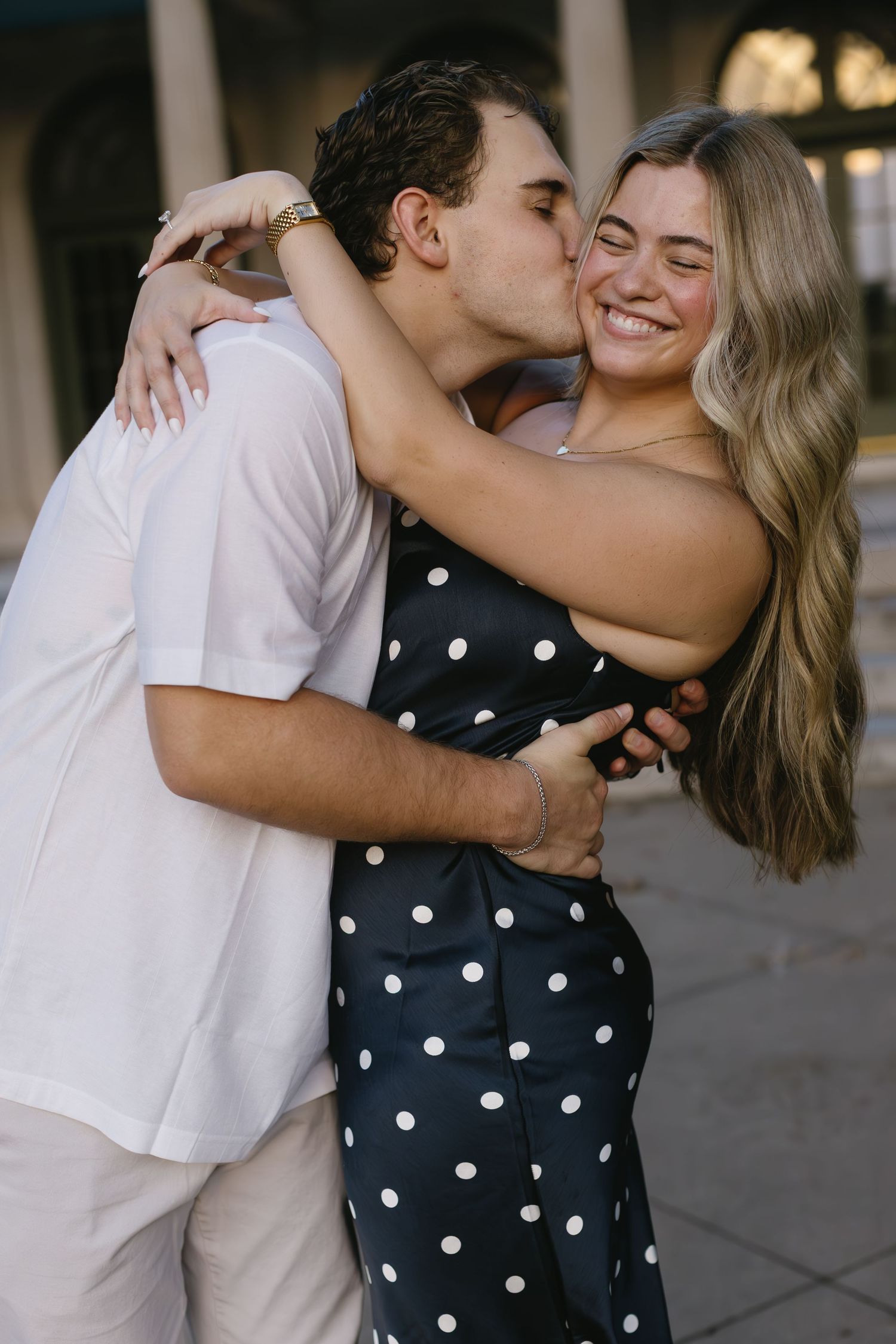 Intimate couple shares romantic embraces and kisses in front of a classical building.