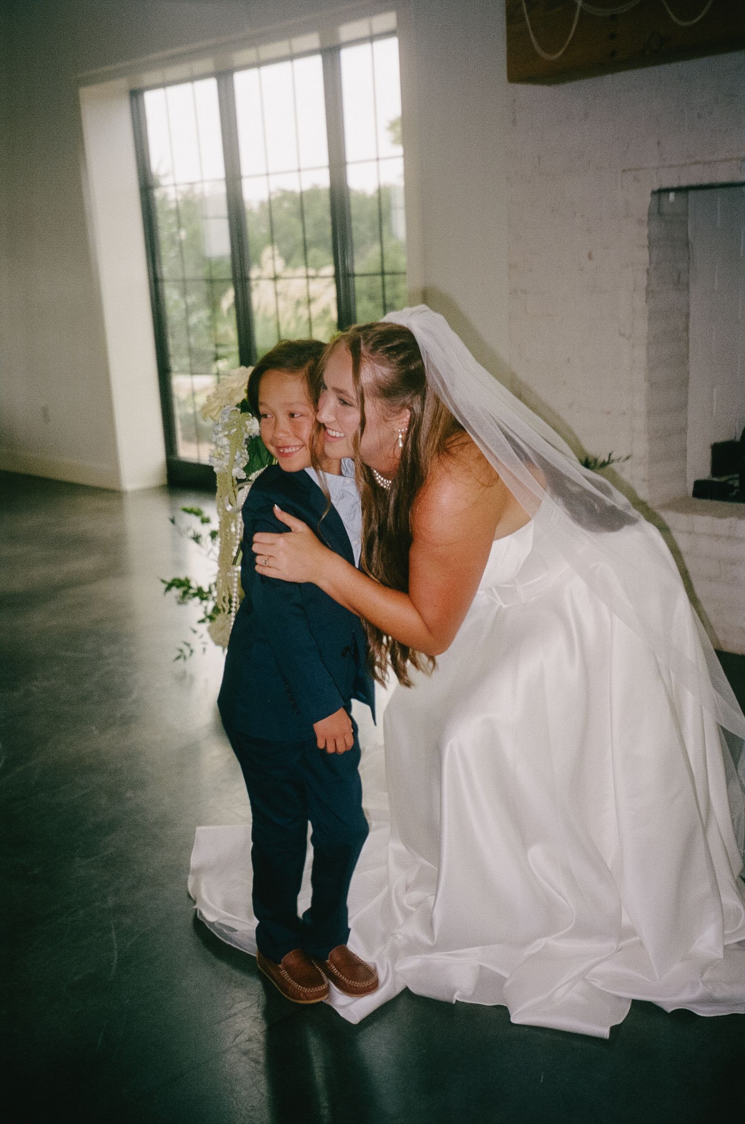 Sweet moment showing a small boy in formal attire sharing a tender embrace with bride in white wedding gown.