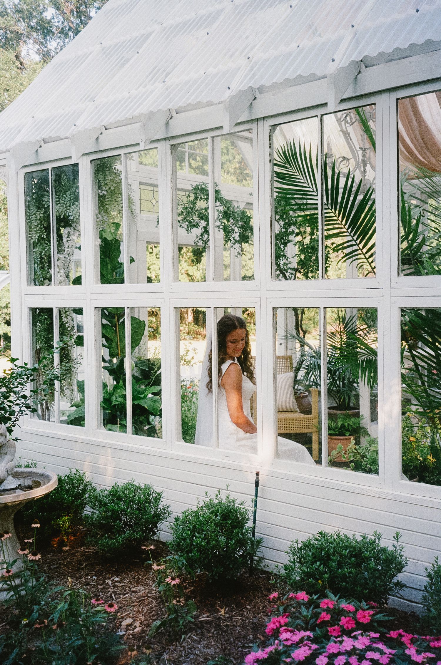 An elegant greenhouse wedding venue with white frame windows, pink flowers, and tropical plants.