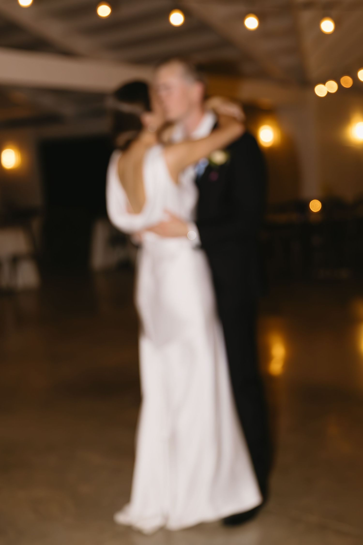 Couple dancing under warm string lights in a romantic wedding reception setting.