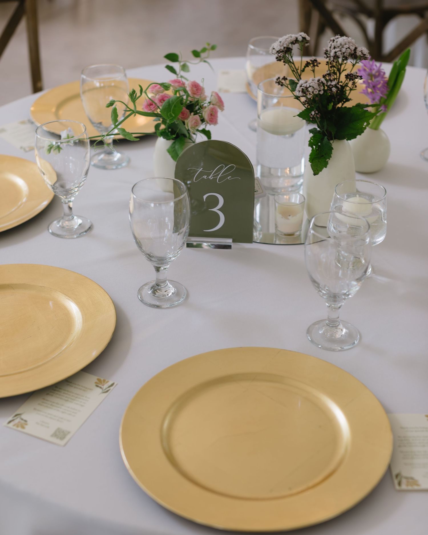Wedding reception table settings with gold charger plates, wine glasses and table numbers.