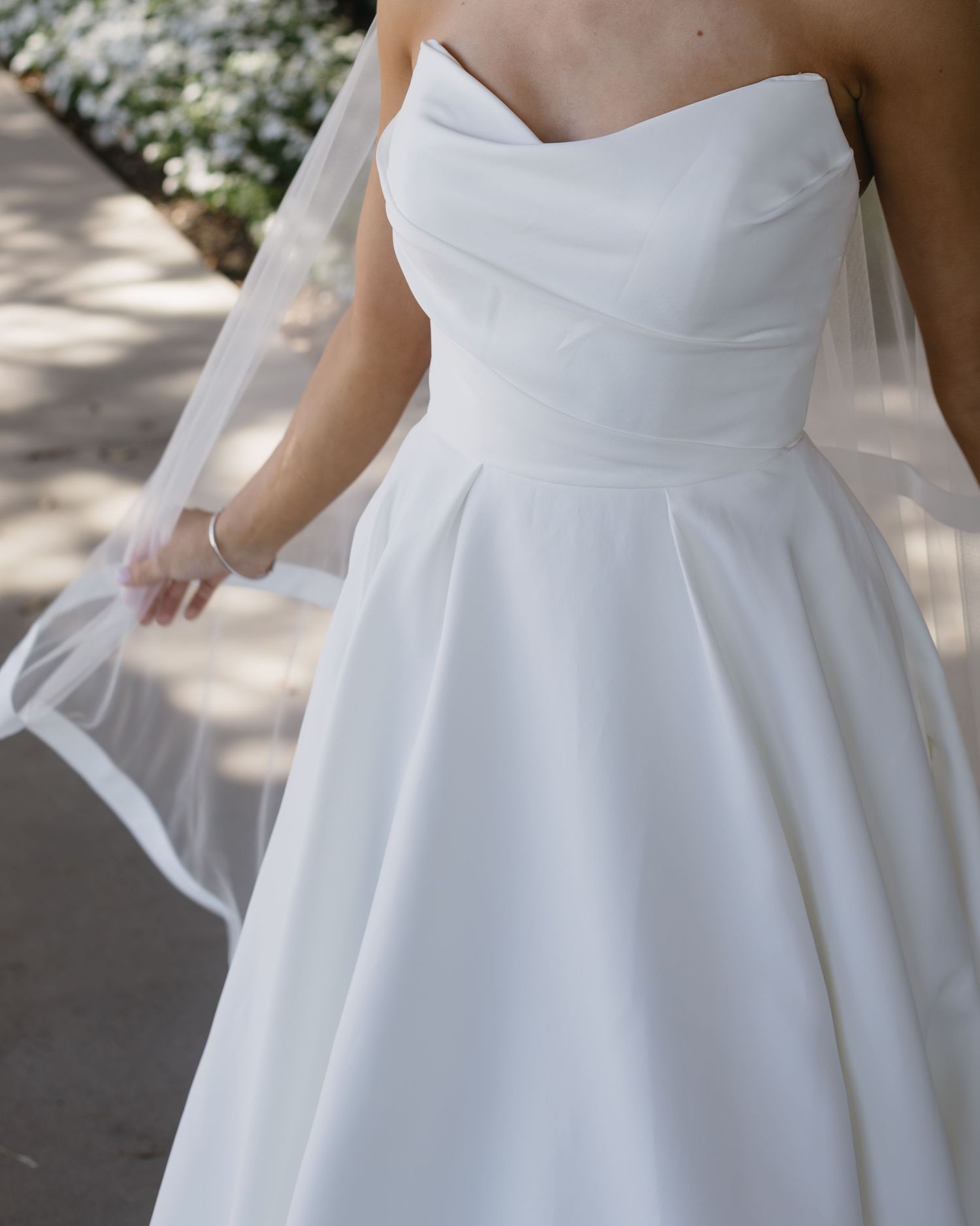 Close-up detail of a classic white wedding gown with sweetheart neckline and pleated skirt.