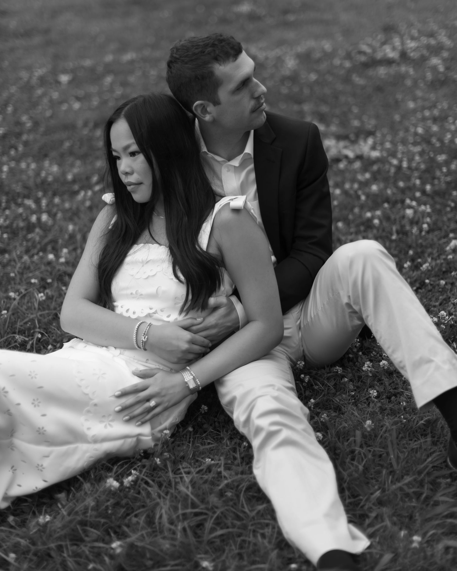 Black and white series shows couple embracing on grass, bride in white dress and groom in dark suit.