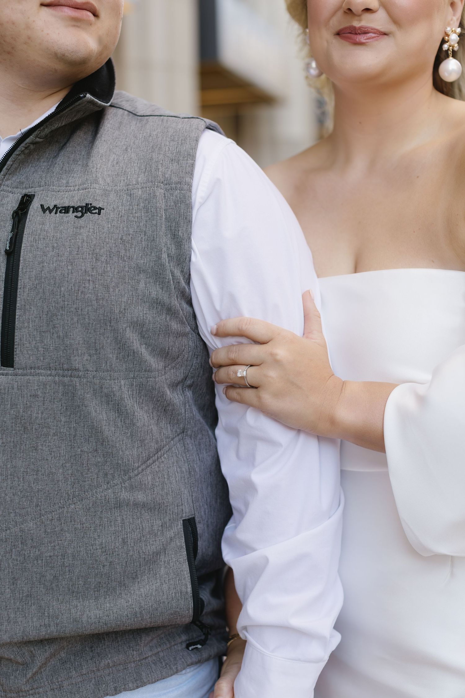 A couple in formal attire embraces against a light colored wall during a photo shoot.