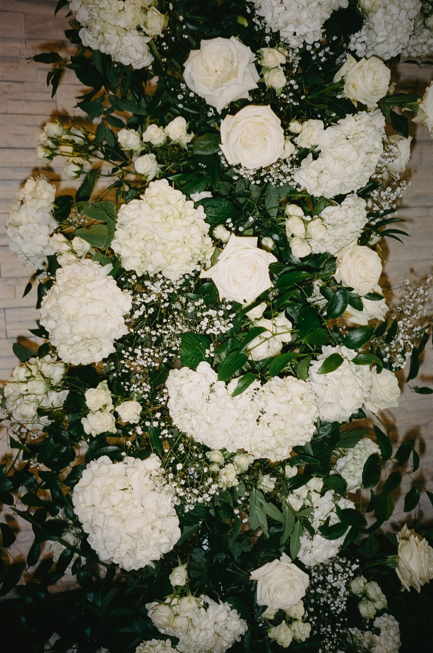 Elegant white floral arrangement featuring roses and hydrangeas adorned with delicate baby's breath against a rustic backdrop.