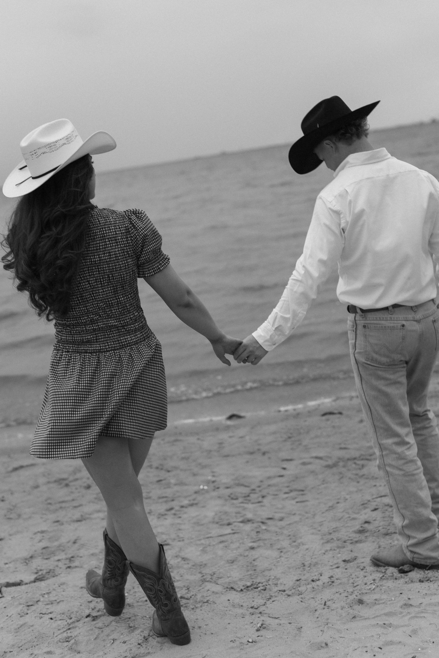 Kids playing and running together on a beach wearing cowboy hats and casual clothes.