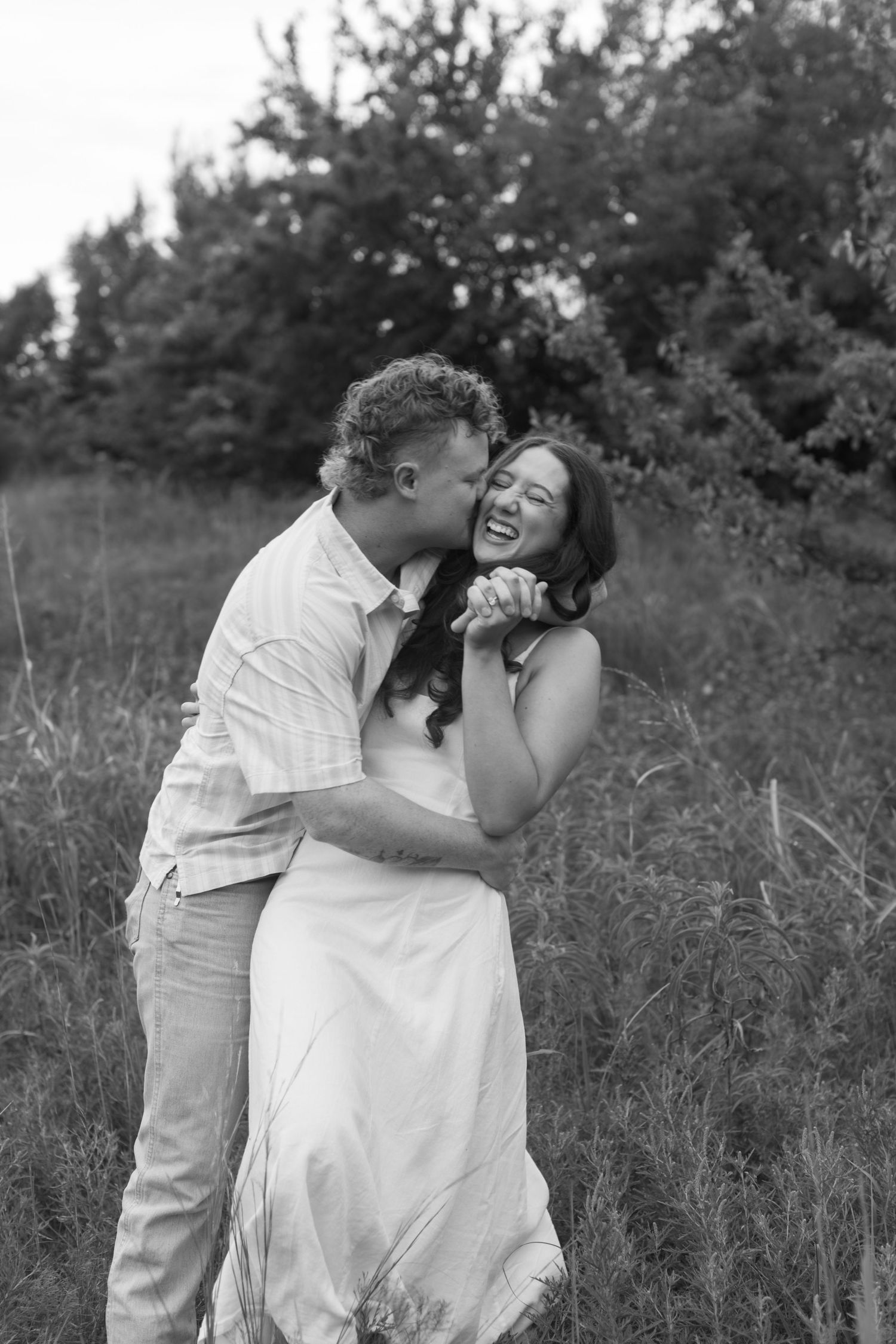 A couple shares an intimate embrace while dancing in a grassy field on a summer day.