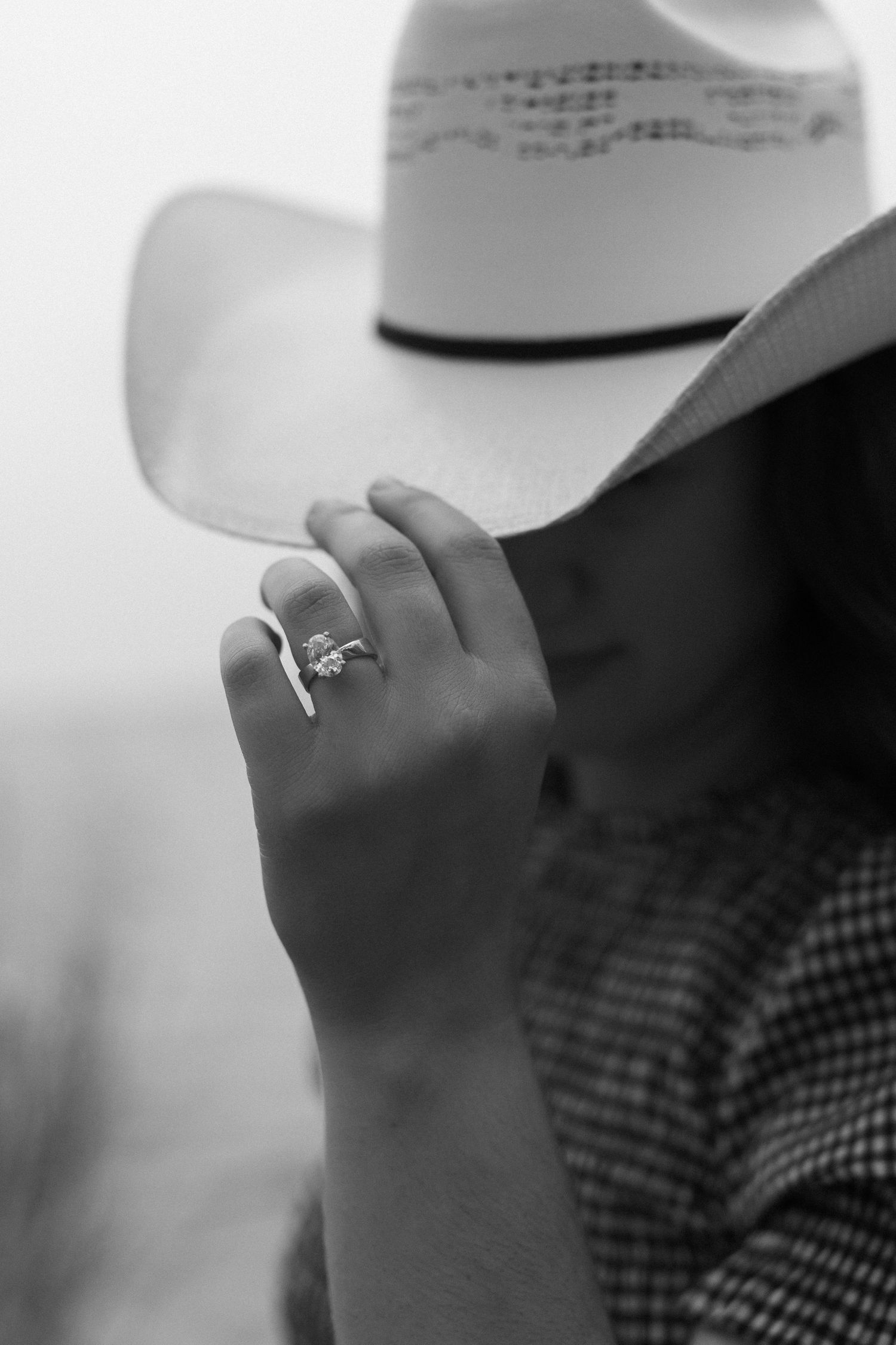 Black and white close-up image shows a person's hand with a ring against a chequered pattern background.