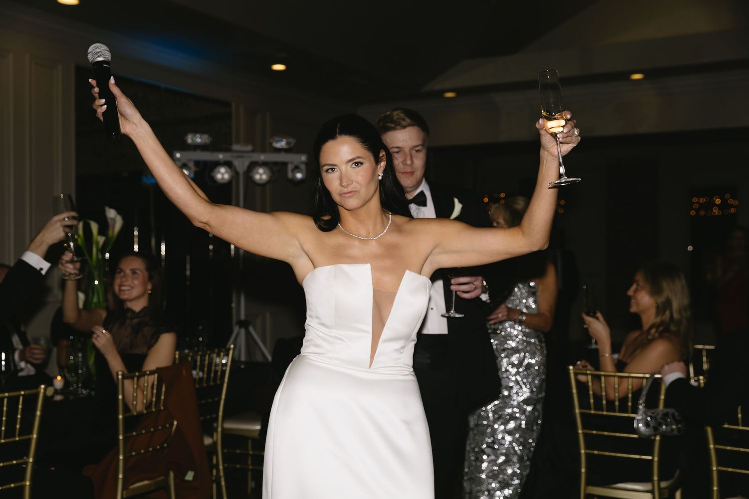 Wedding celebration with dancing and raised arms in dimly lit reception venue.