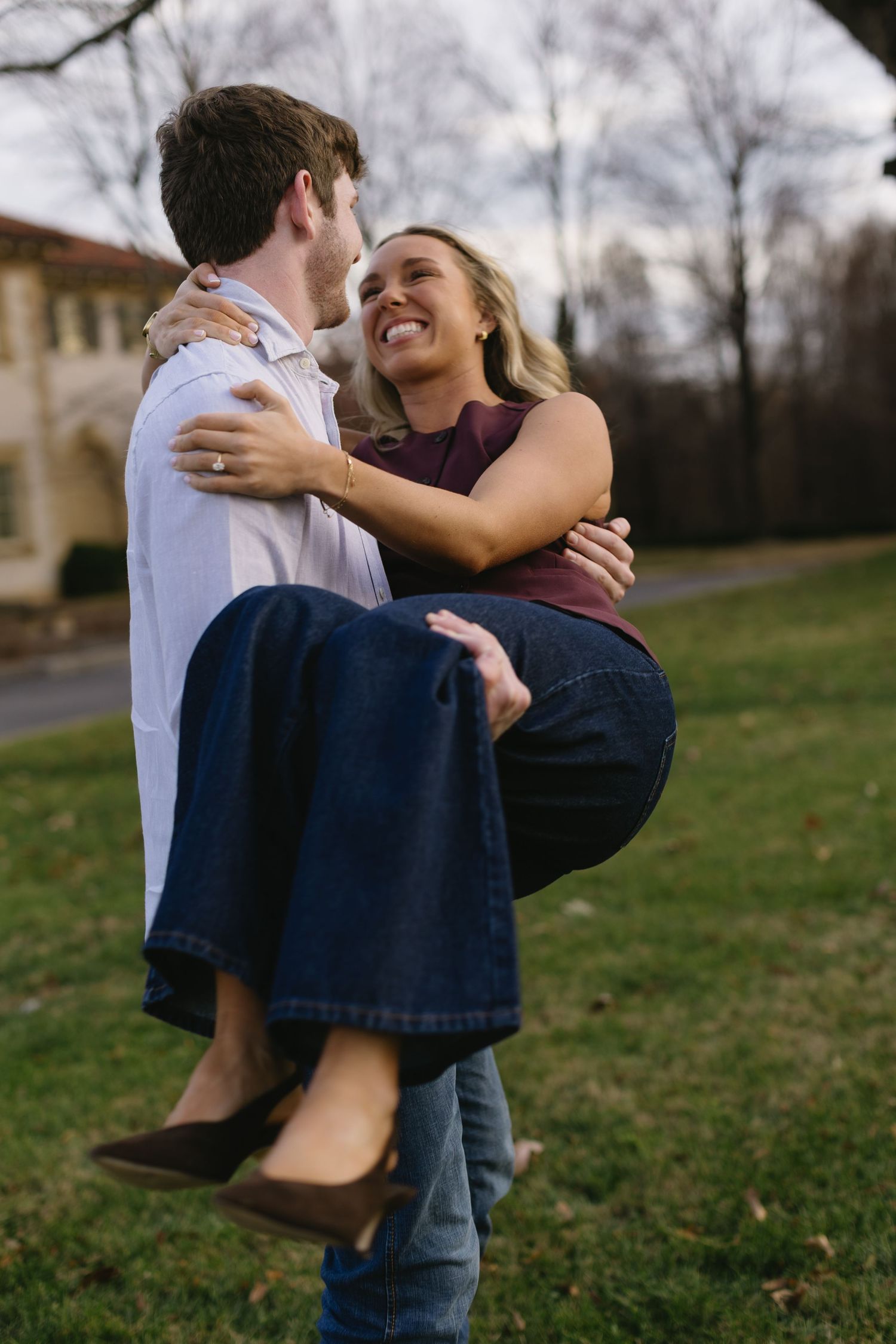 A playful moment captured as a couple embraces on a lawn with one being lifted up.