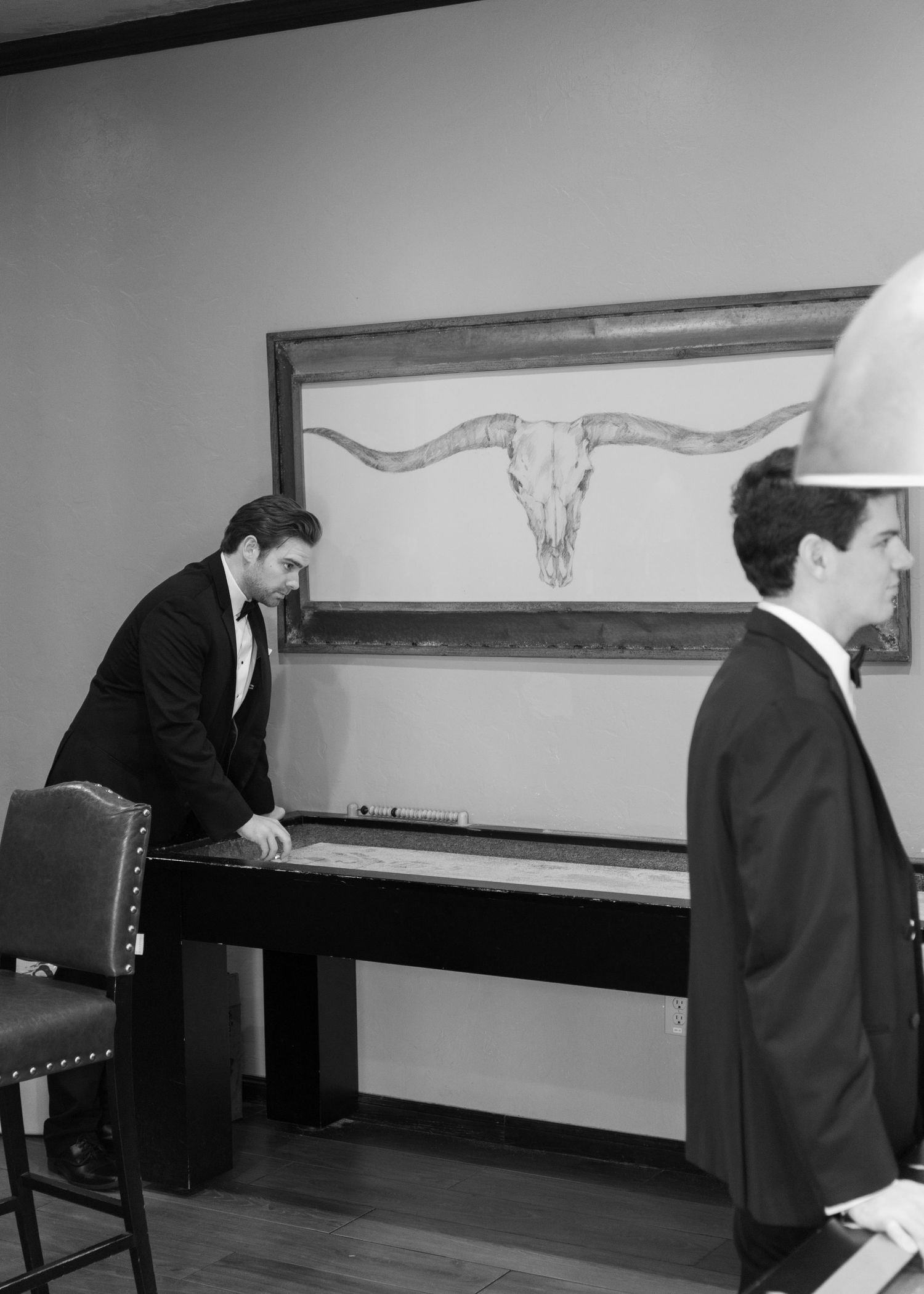 Two people in formal attire sit at a piano in a minimalist room with wall art.
