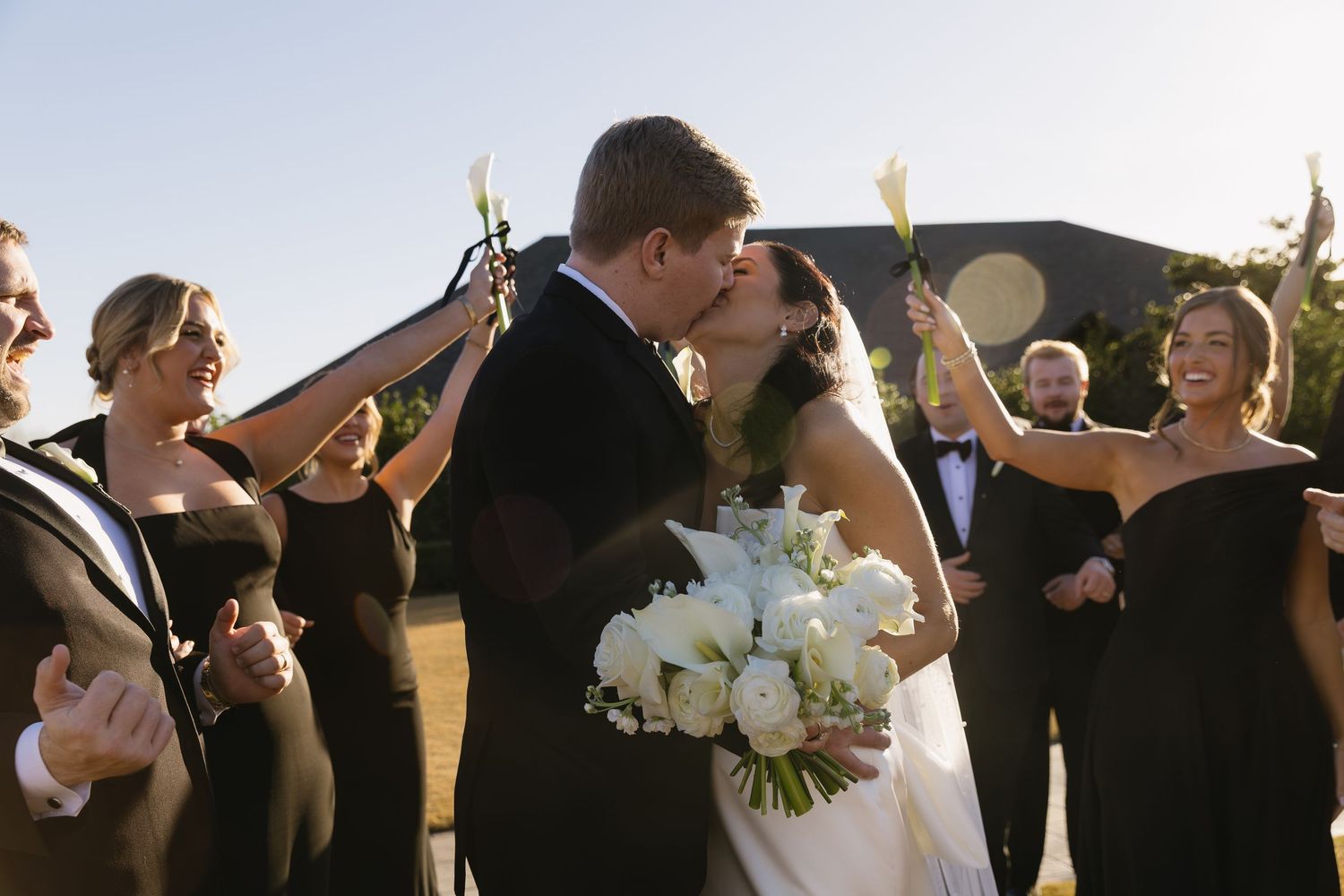 Wedding party celebrates as newlyweds share first kiss at outdoor ceremony.