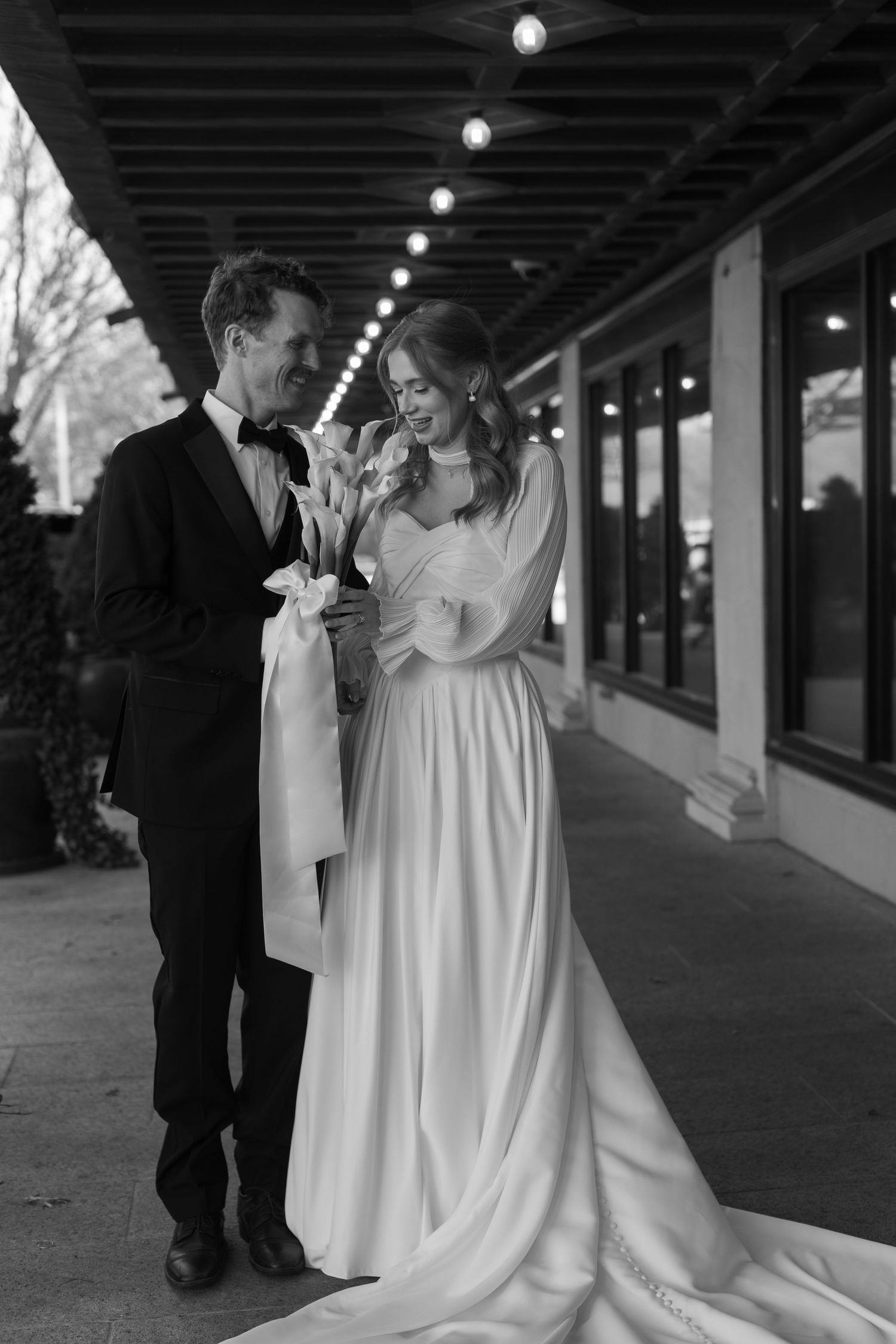Black and white wedding portrait under covered walkway with string lights.