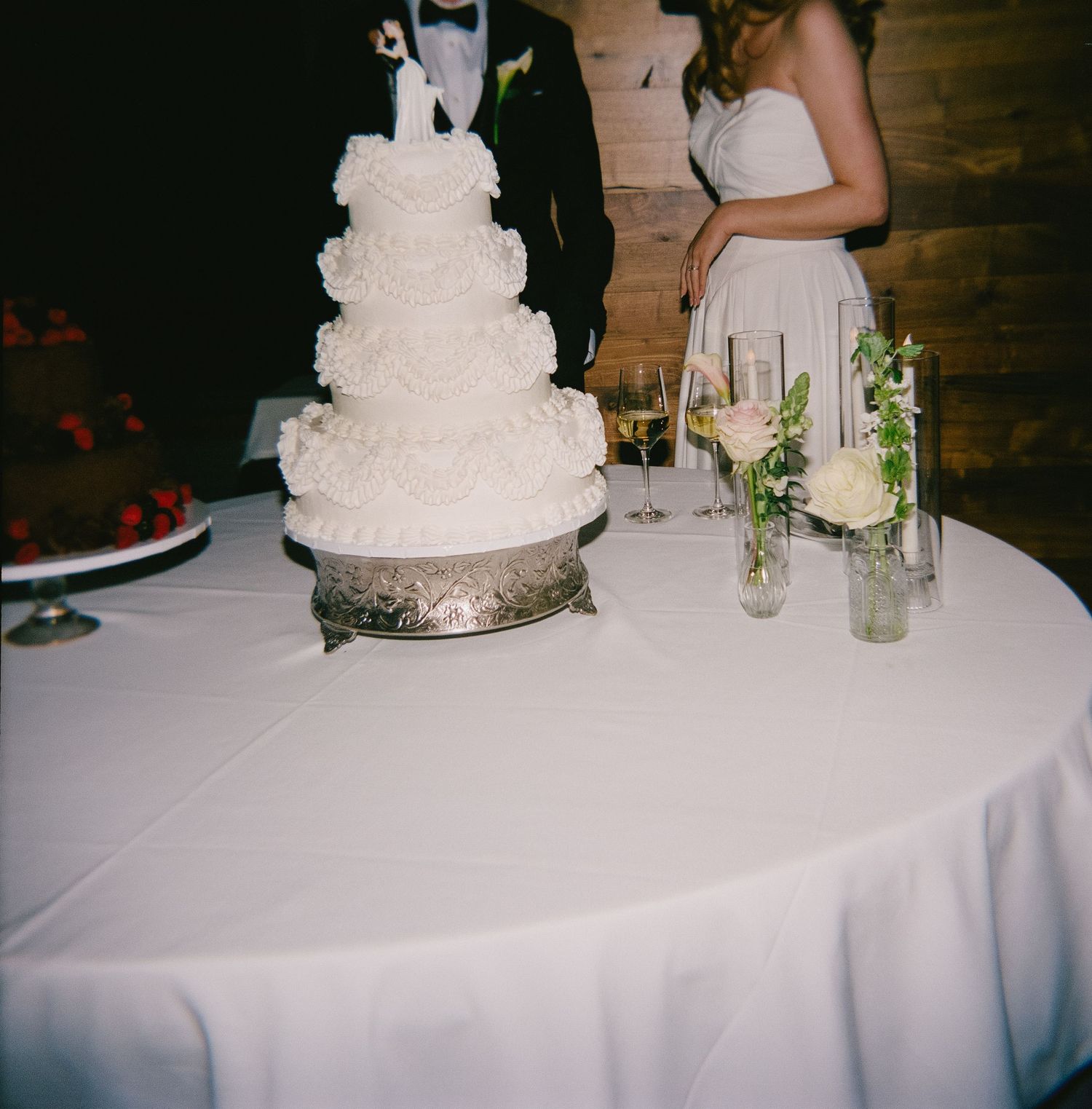 Classic white tiered wedding cake displayed on silver stand with floral accents.