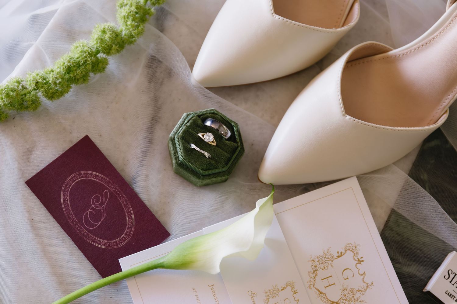 Elegant white bridal shoes and accessories arranged with delicate green floral accents.