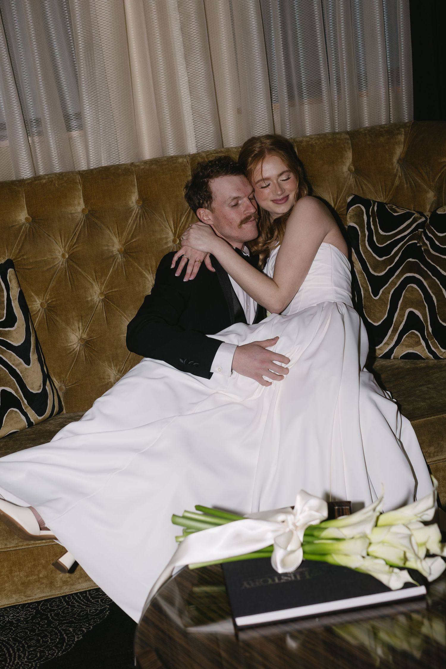 Couple relaxes on vintage velvet couch with white calla lilies in foreground.