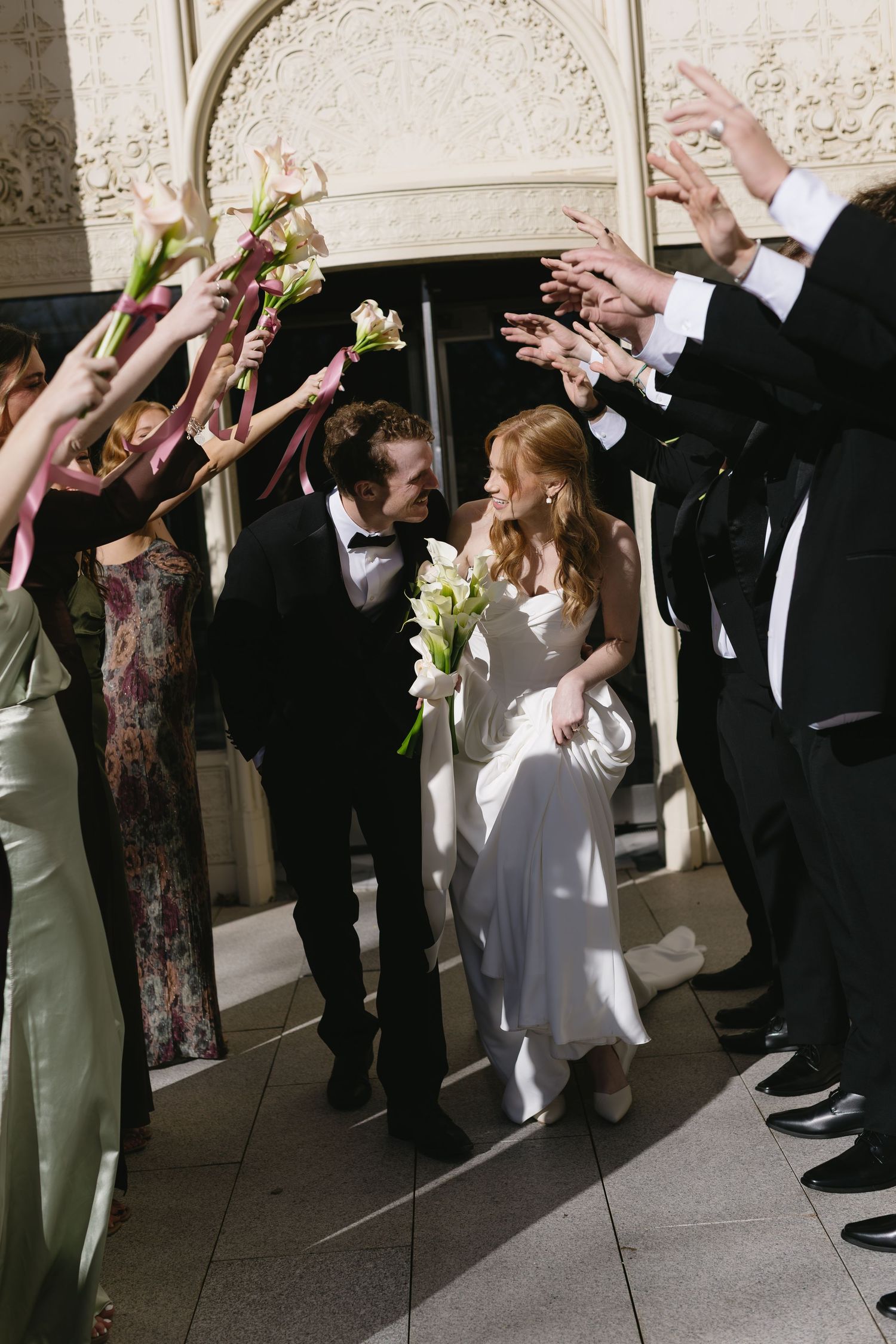 Wedding party members form an archway with their arms in formal attire.