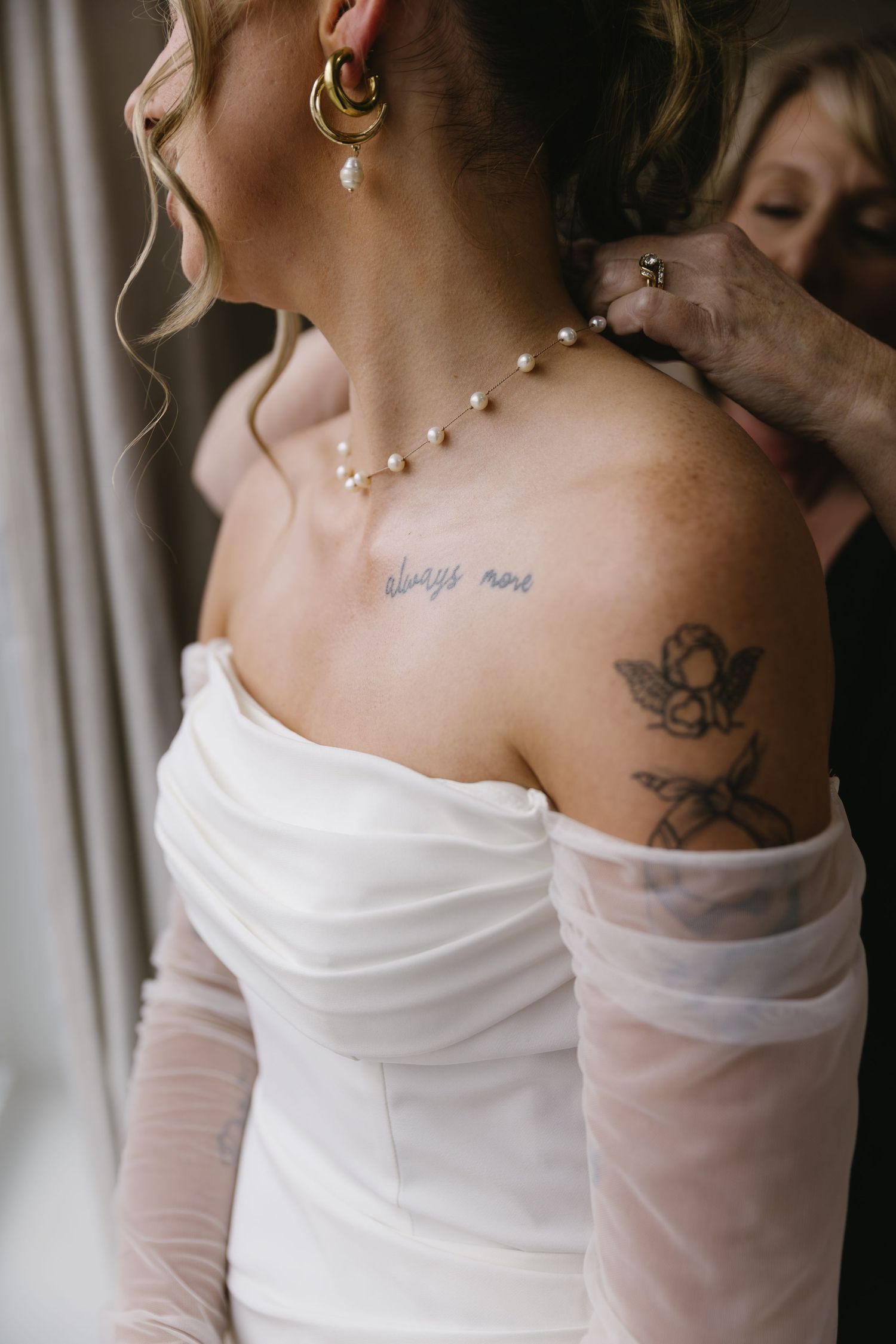 Close-up view of a bride's back showing delicate pearl necklace and shoulder tattoos in an elegant white gown.