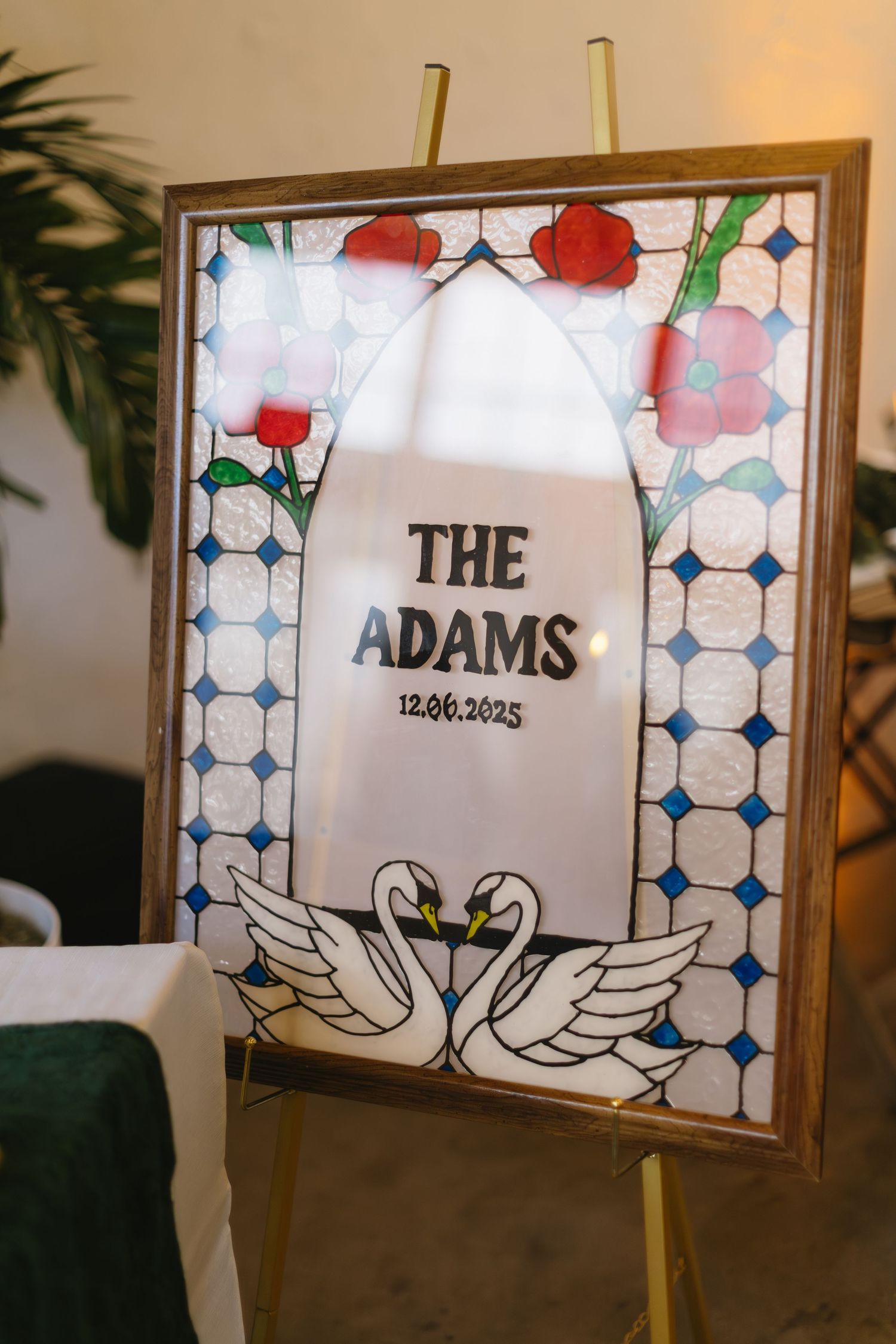 A framed wedding sign with 'The Adams' text decorated with red roses and swan illustrations.