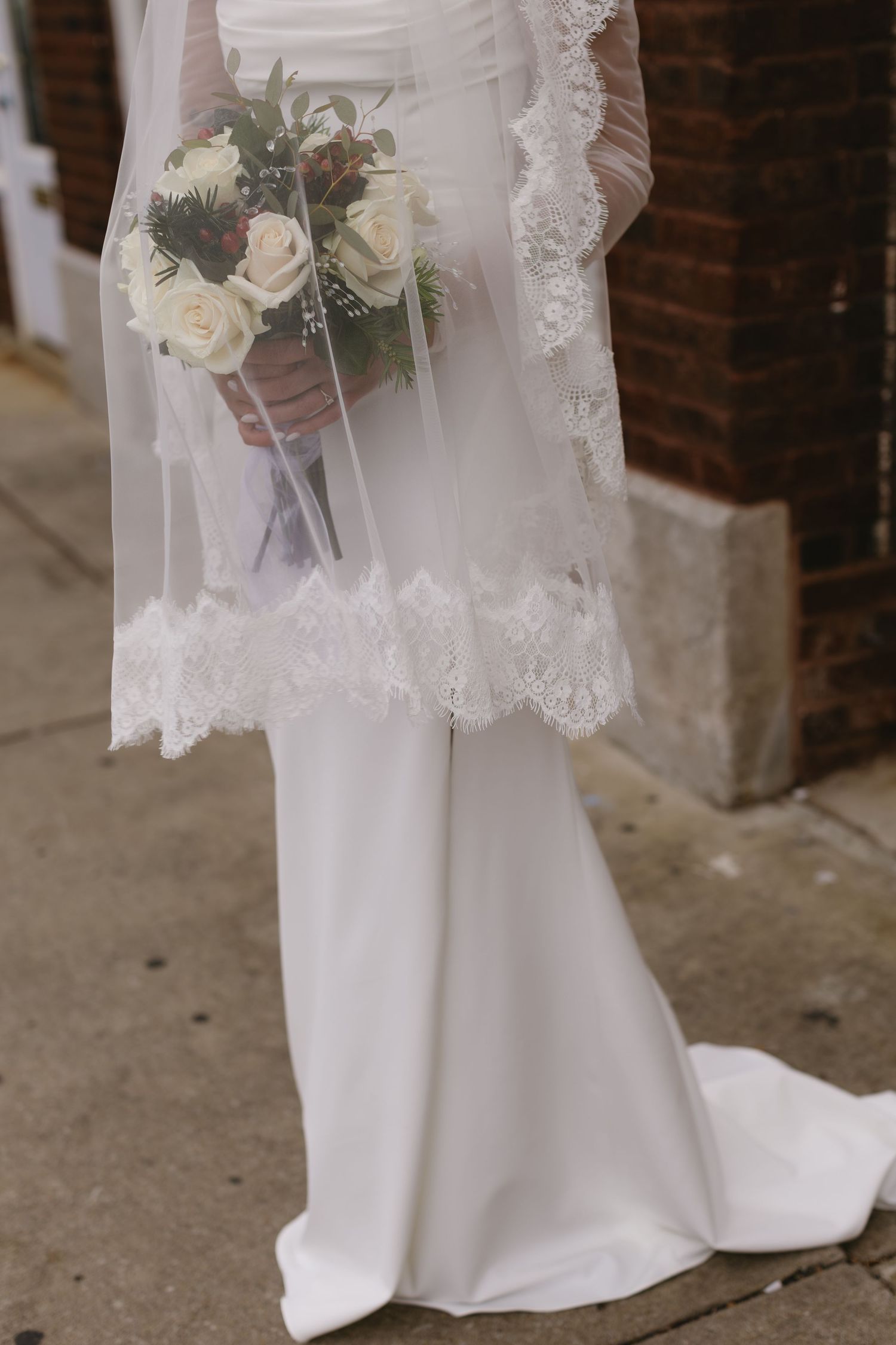 Close-up of a white wedding dress with lace veil and delicate floral bouquet.