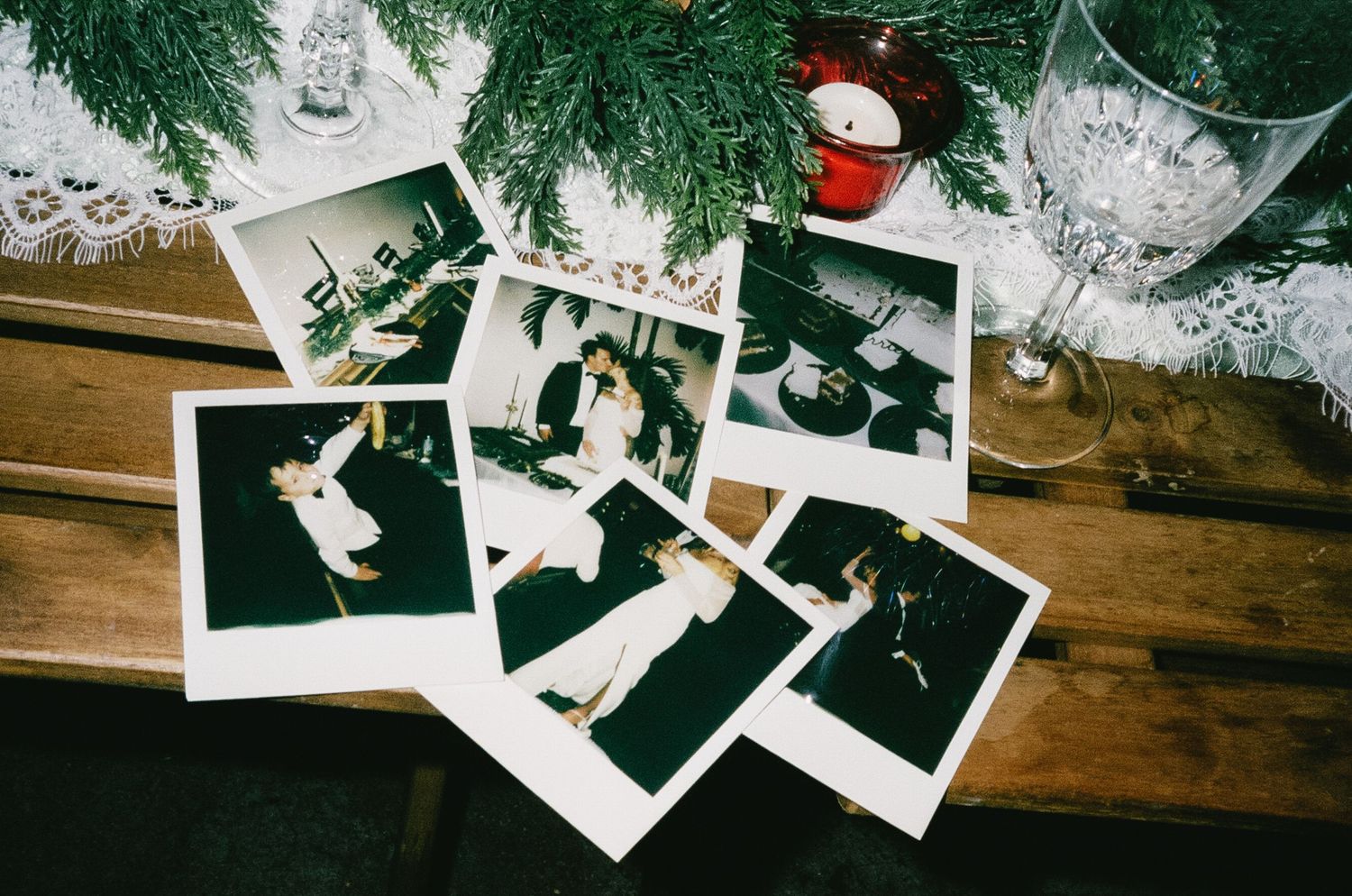 Polaroid photographs scattered among pine branches and Christmas decorations on a wooden surface.