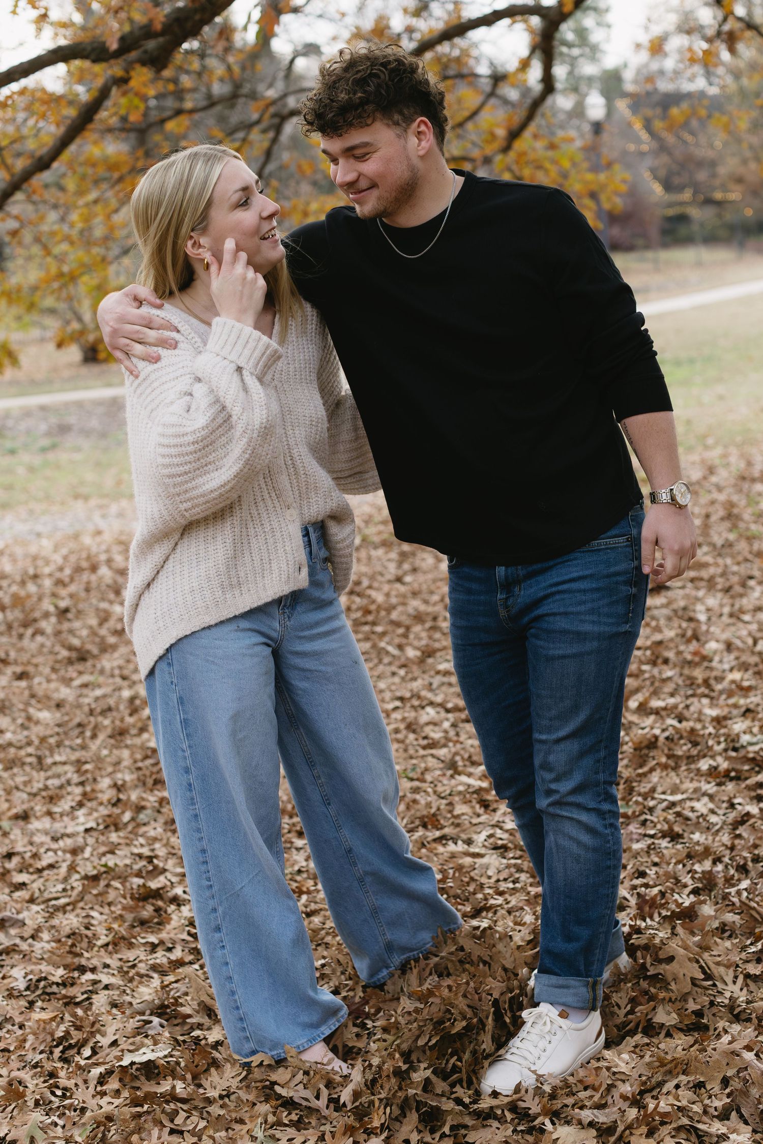 A playful autumn photoshoot of a couple in coordinated sweaters among fallen leaves.
