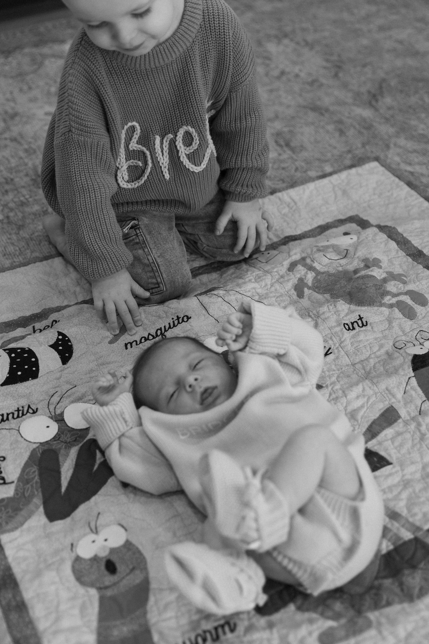 A child in a sweater plays with a baby doll on a patterned mat during playtime.