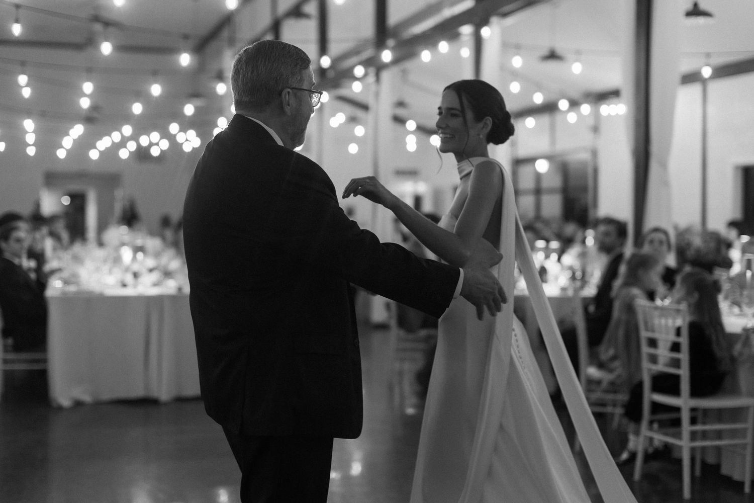 Wedding reception venue decorated with string lights as couple shares first dance.