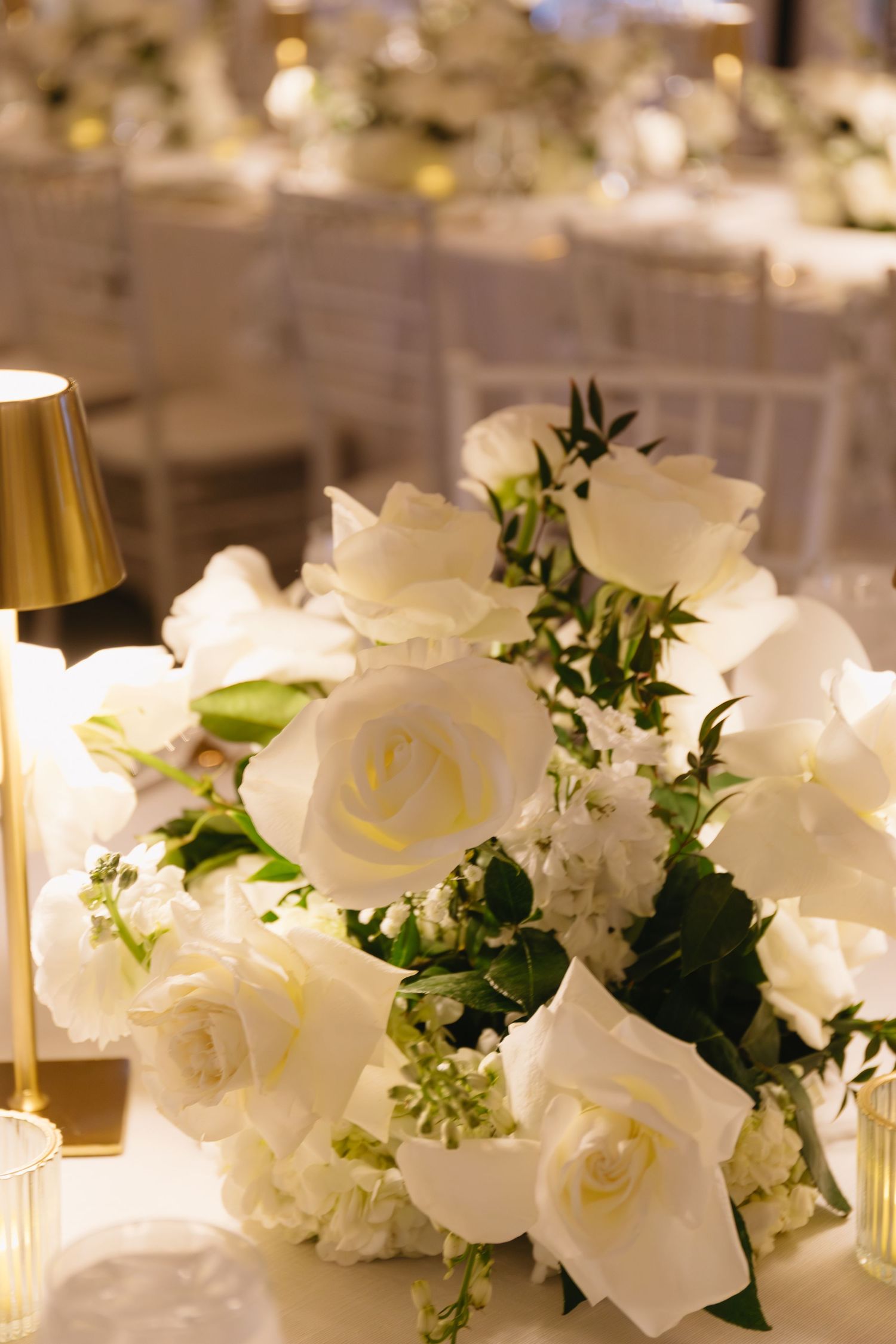 Elegant white floral centerpieces with roses and greenery on wedding reception tables.