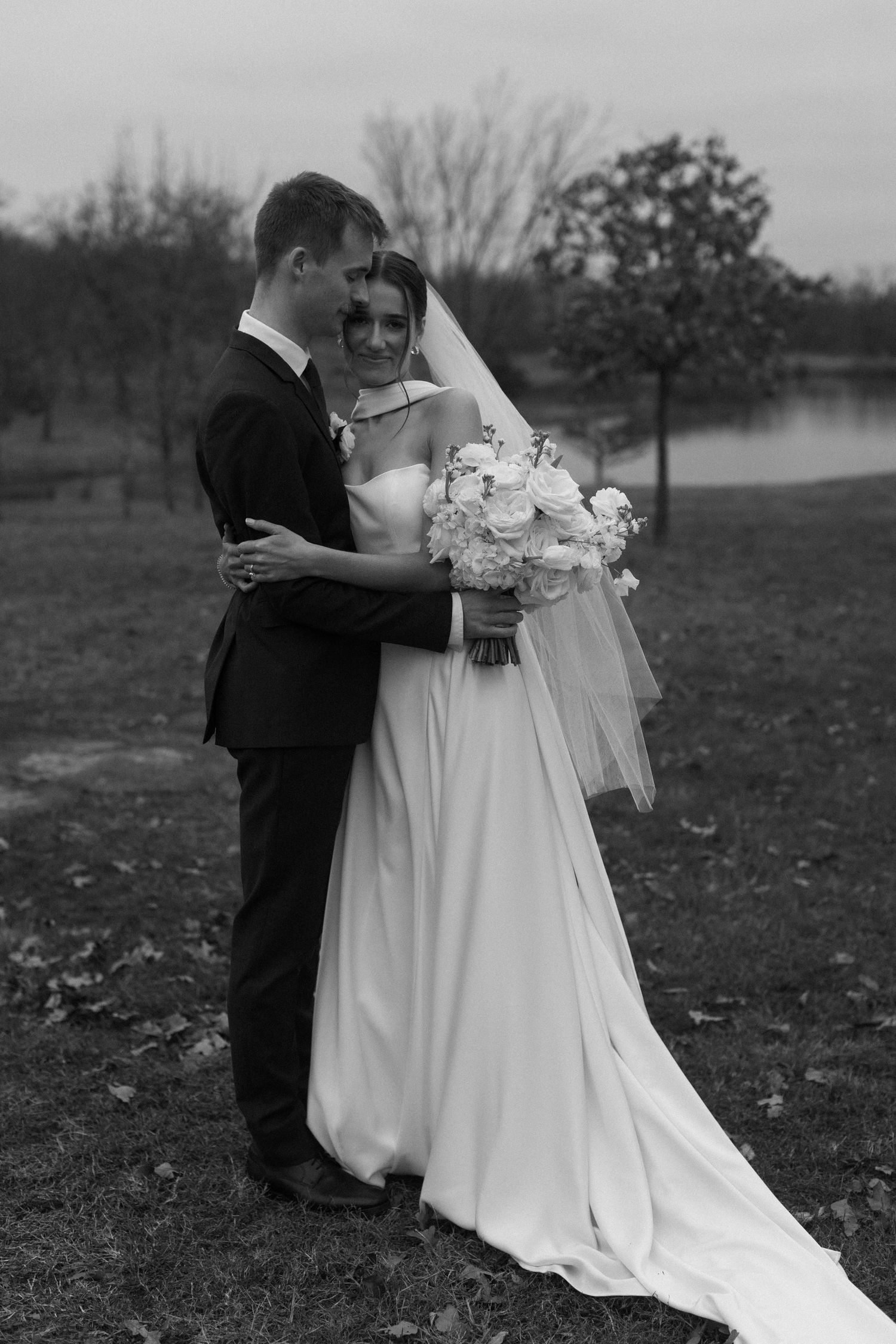 A romantic black and white photo of newlyweds embracing in a field.